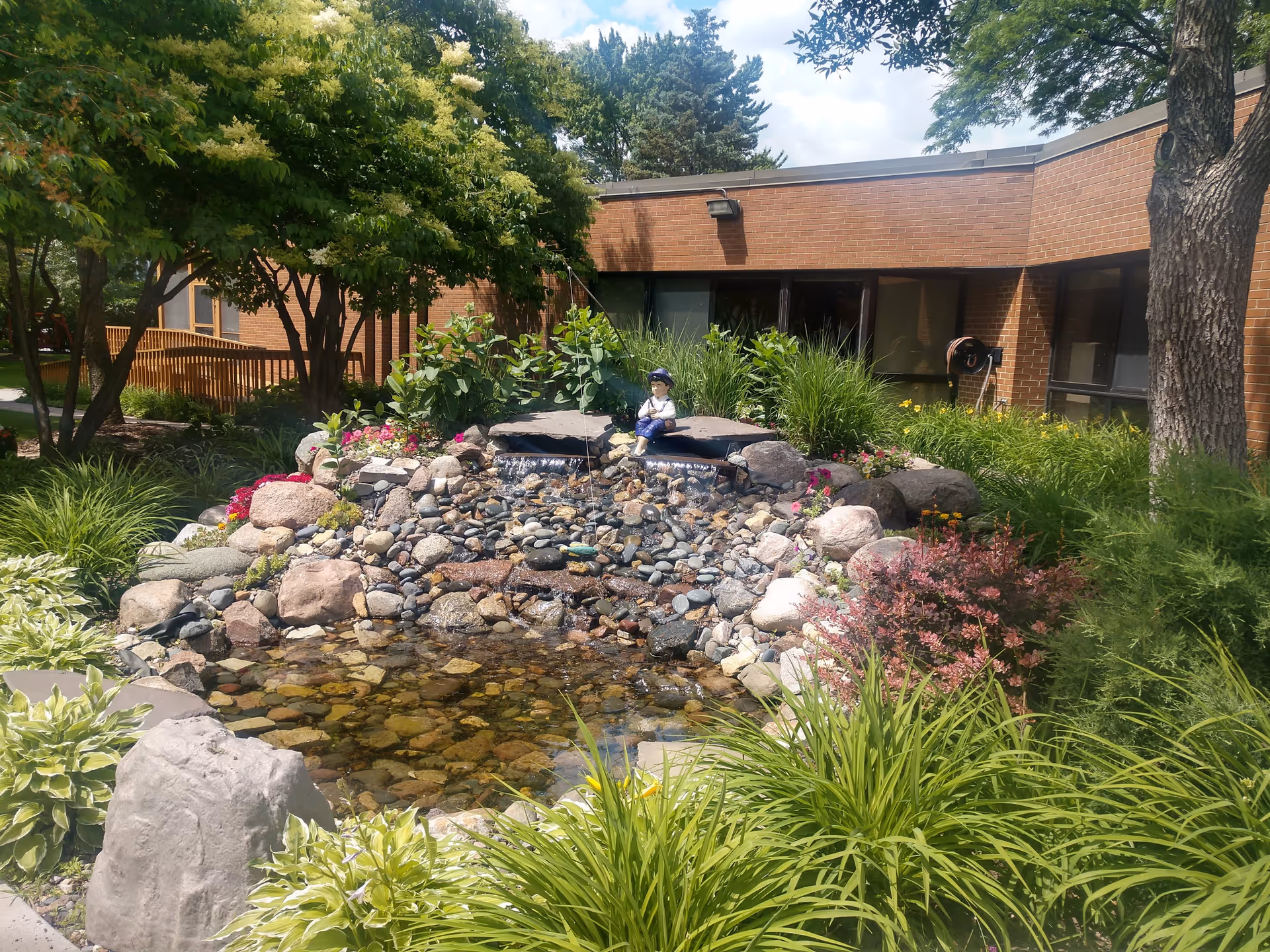 A landscaped outdoor courtyard with a rock pond, plants, and brick building in background.