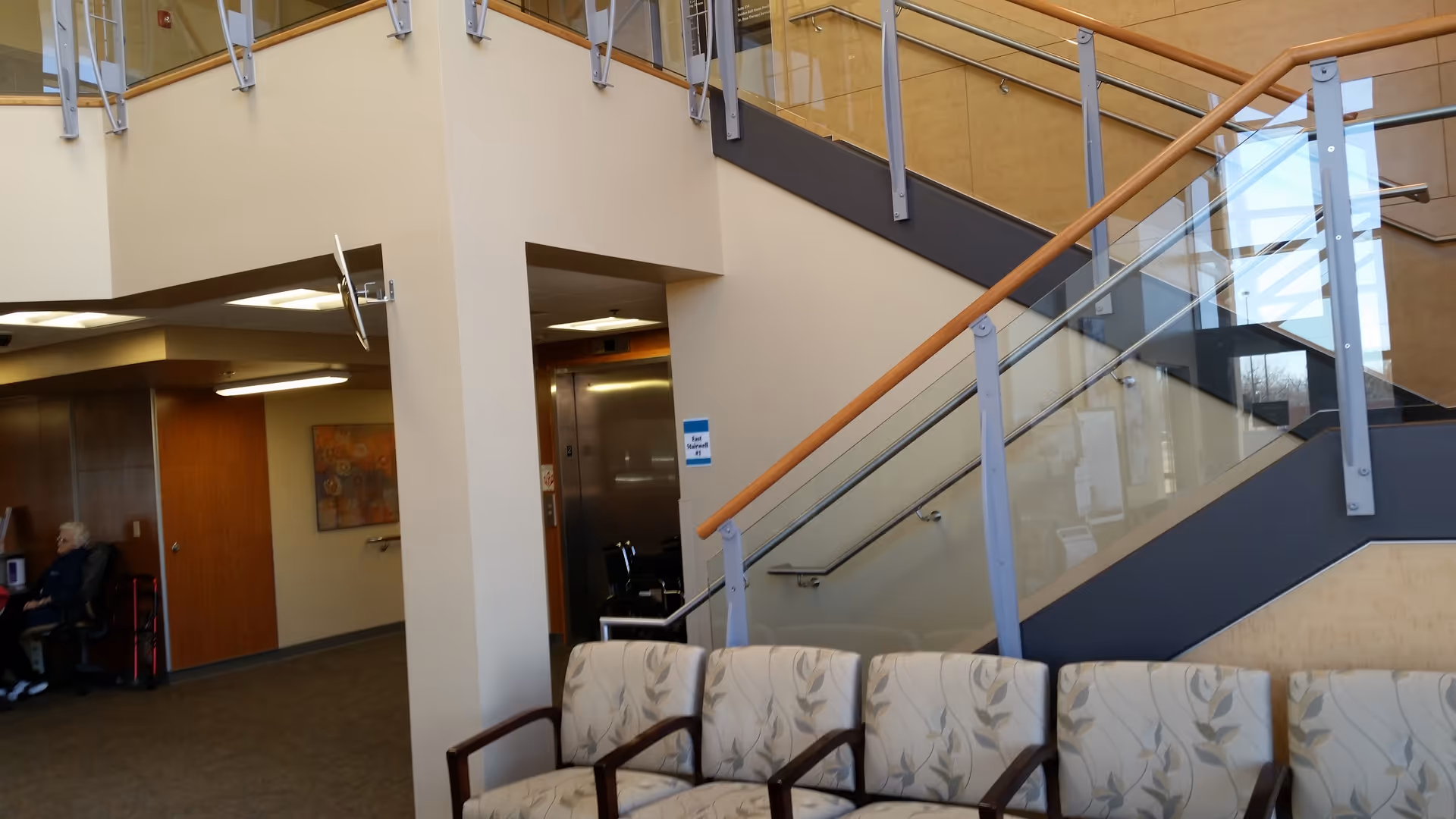Interior atrium of St. Rose Health Center with staircase, elevator, and seating.
