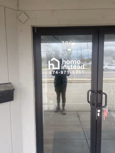 Glass door entrance displaying Home Instead logo, 306; reflection of person in doorway.