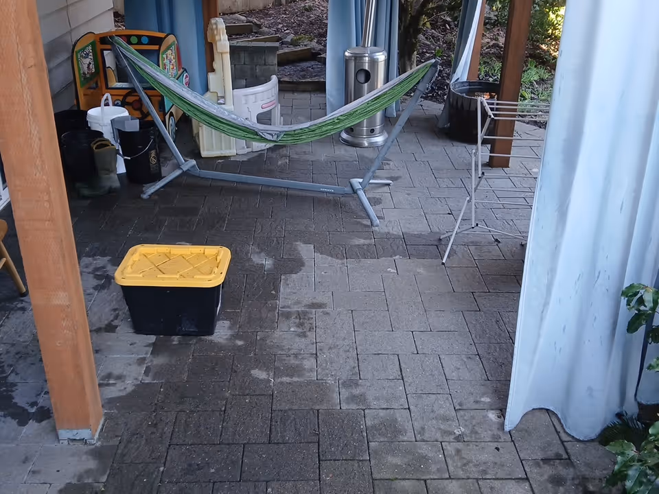 Outdoor patio area with a green hammock, drying rack, yellow-lidded bin, and pavers.