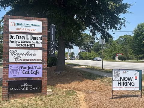 Exterior view of Right at Home sign with neighboring storefronts and a Now Hiring sign.