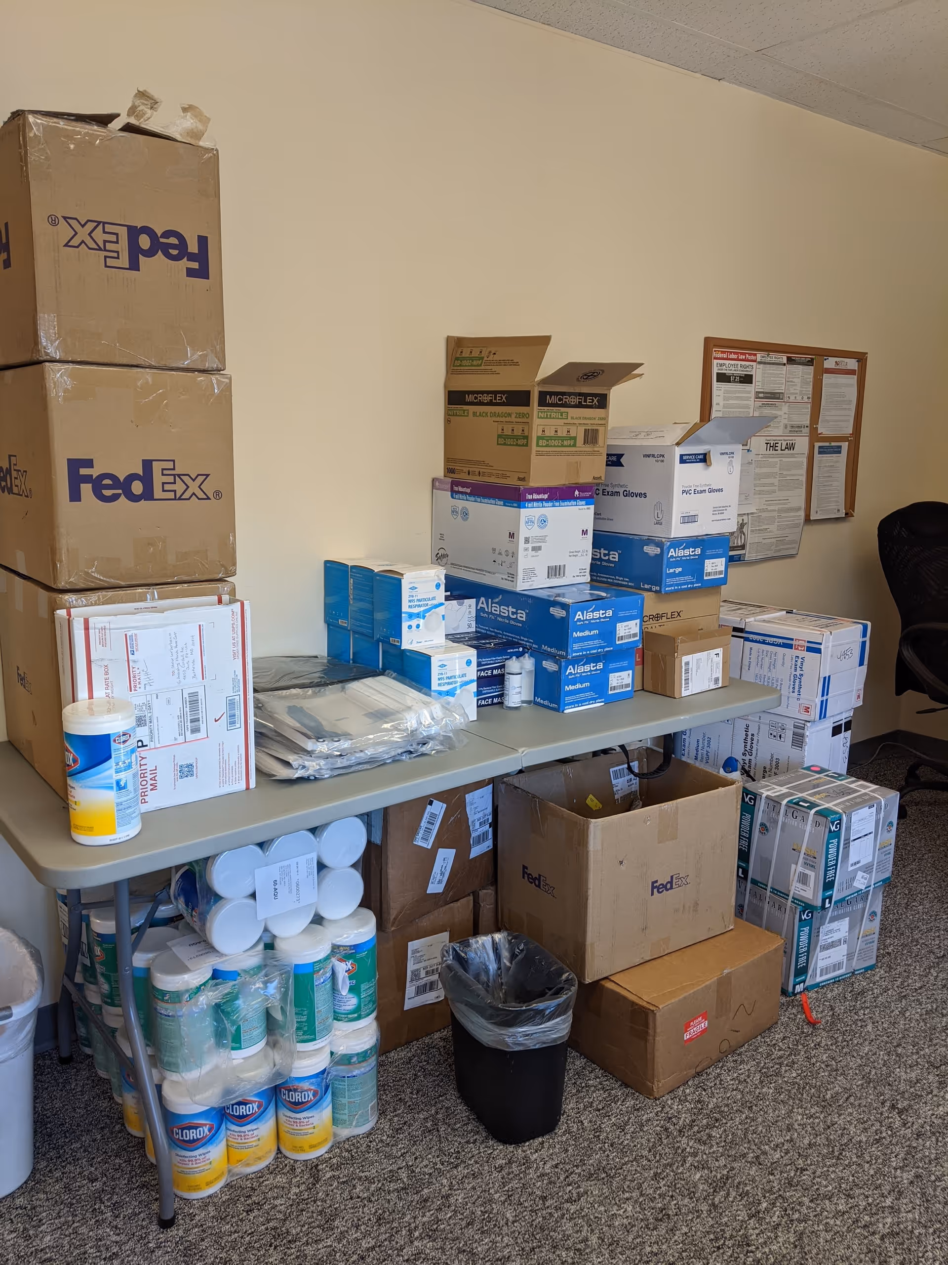 Storage area with boxes and medical supplies stacked on a table in an office room.
