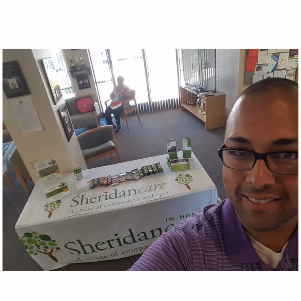 Selfie of a man in a purple polo at a Sheridan care table inside a lobby.