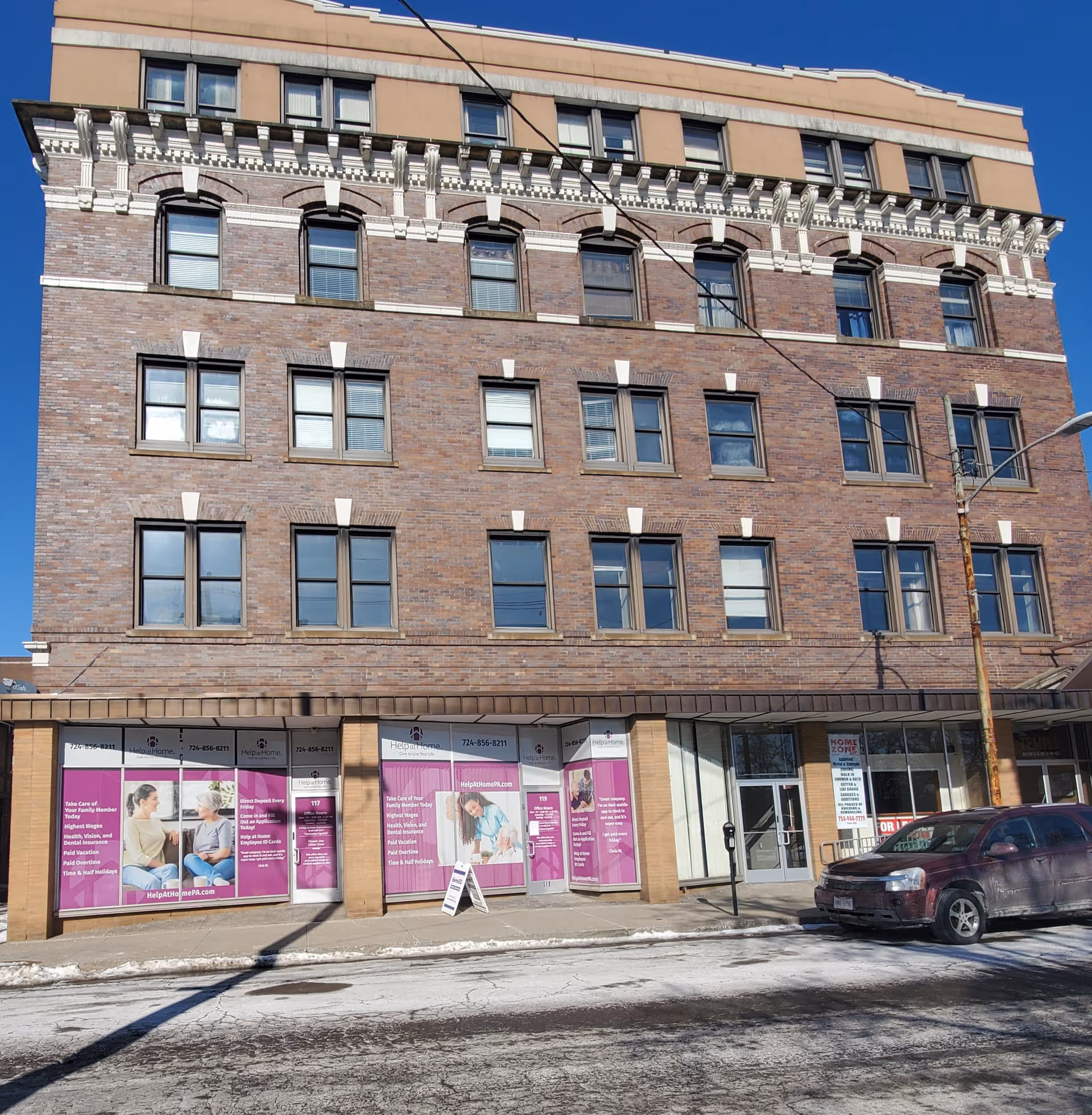 Brick four-story building with purple storefront signs advertising Help at Home on the ground level.