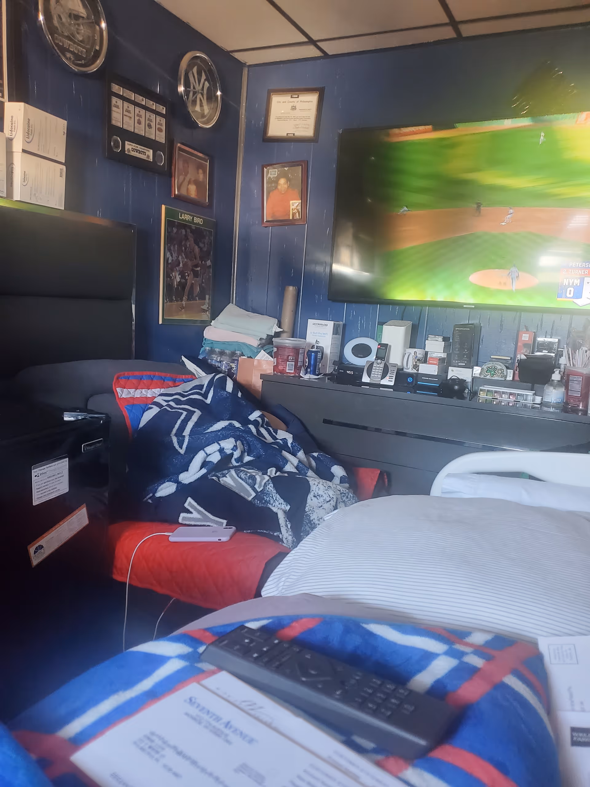 Cozy, cluttered bedroom in a senior care setting with a TV, blankets, and scattered belongings.