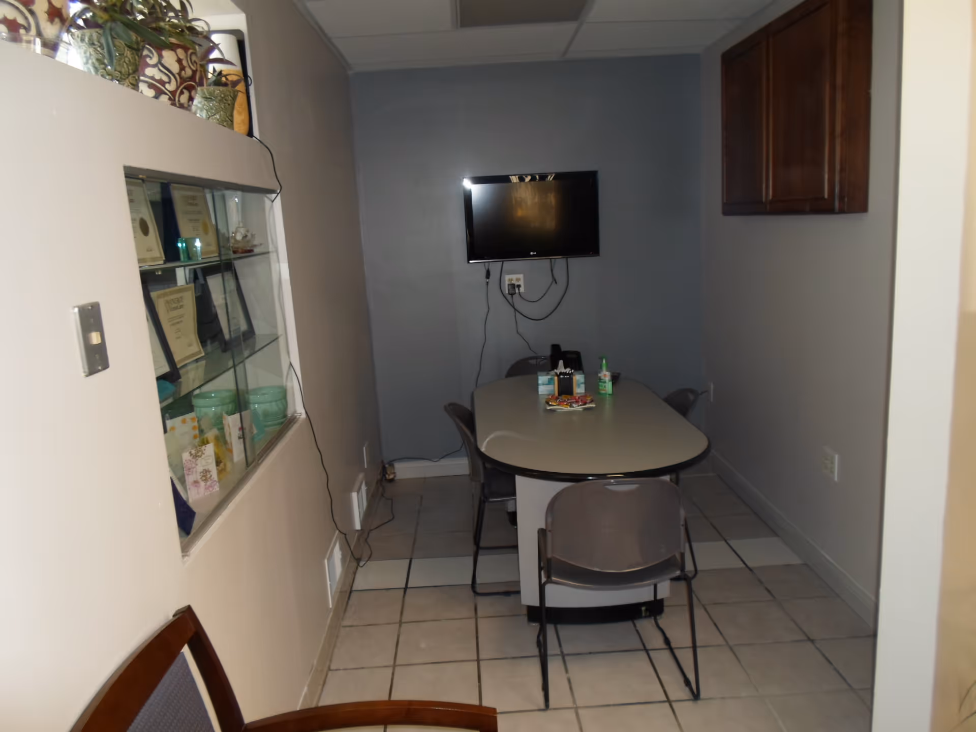 A small interior dining room with a table, chairs, TV, and glass display cabinet.