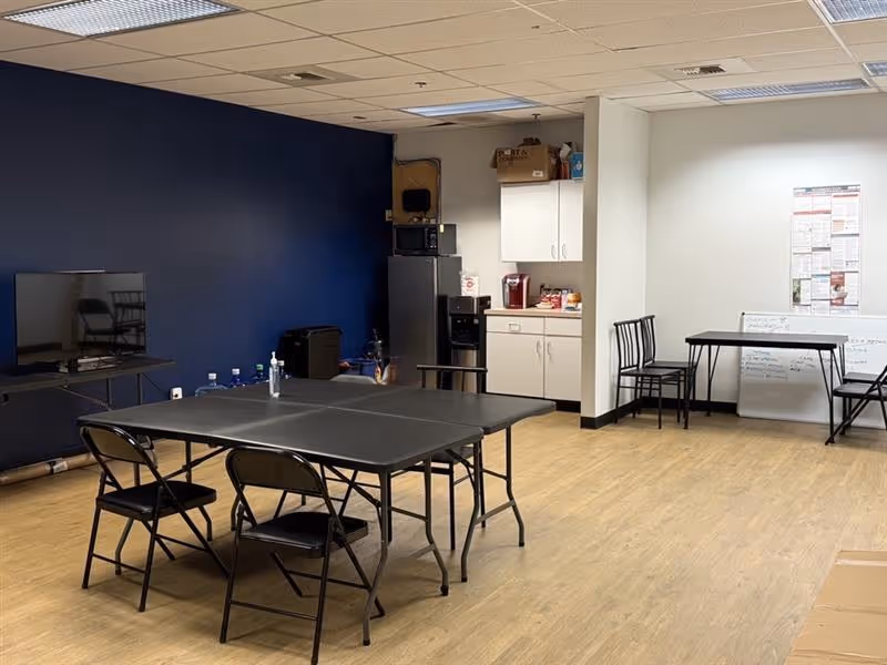 Interior room with black folding tables, chairs, and a kitchenette against a blue wall.