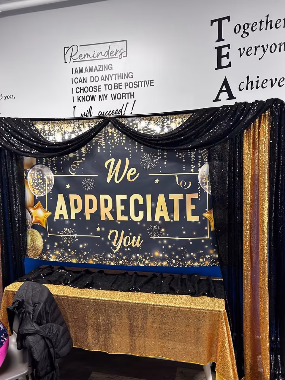Indoor event setup with gold and black We Appreciate You banner and draped backdrop.
