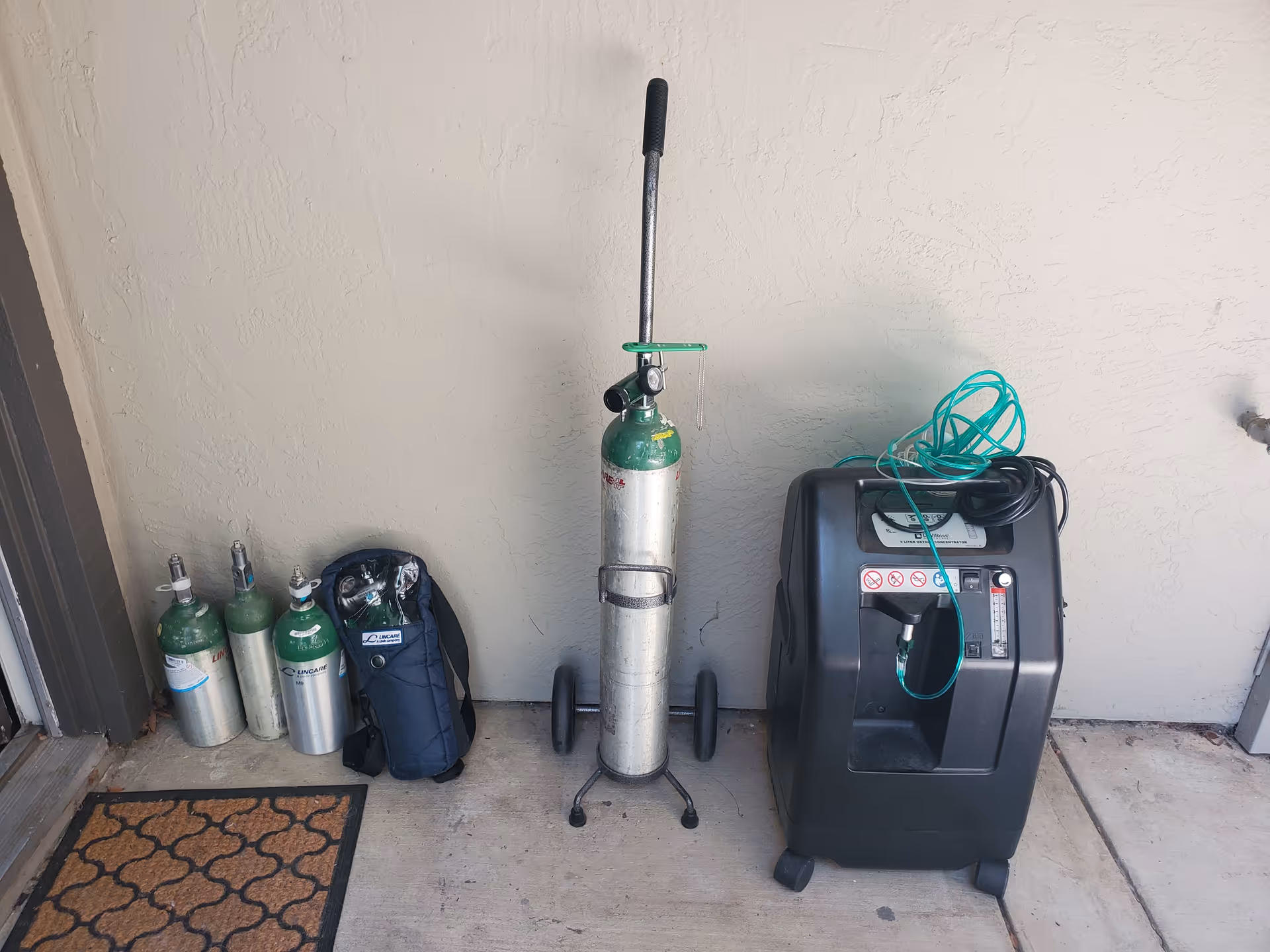 Outdoor utility area with multiple oxygen tanks, a wheeled oxygen cart, and a concentrator.