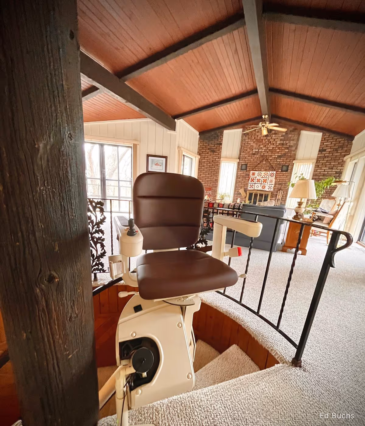A brown stairlift chair mounted beside a curved staircase in a cozy brick-walled living area.