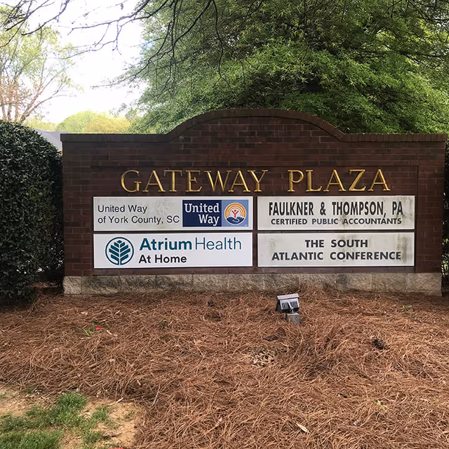 Outdoor brick gateway plaza sign displaying tenant logos including Atrium Health At Home