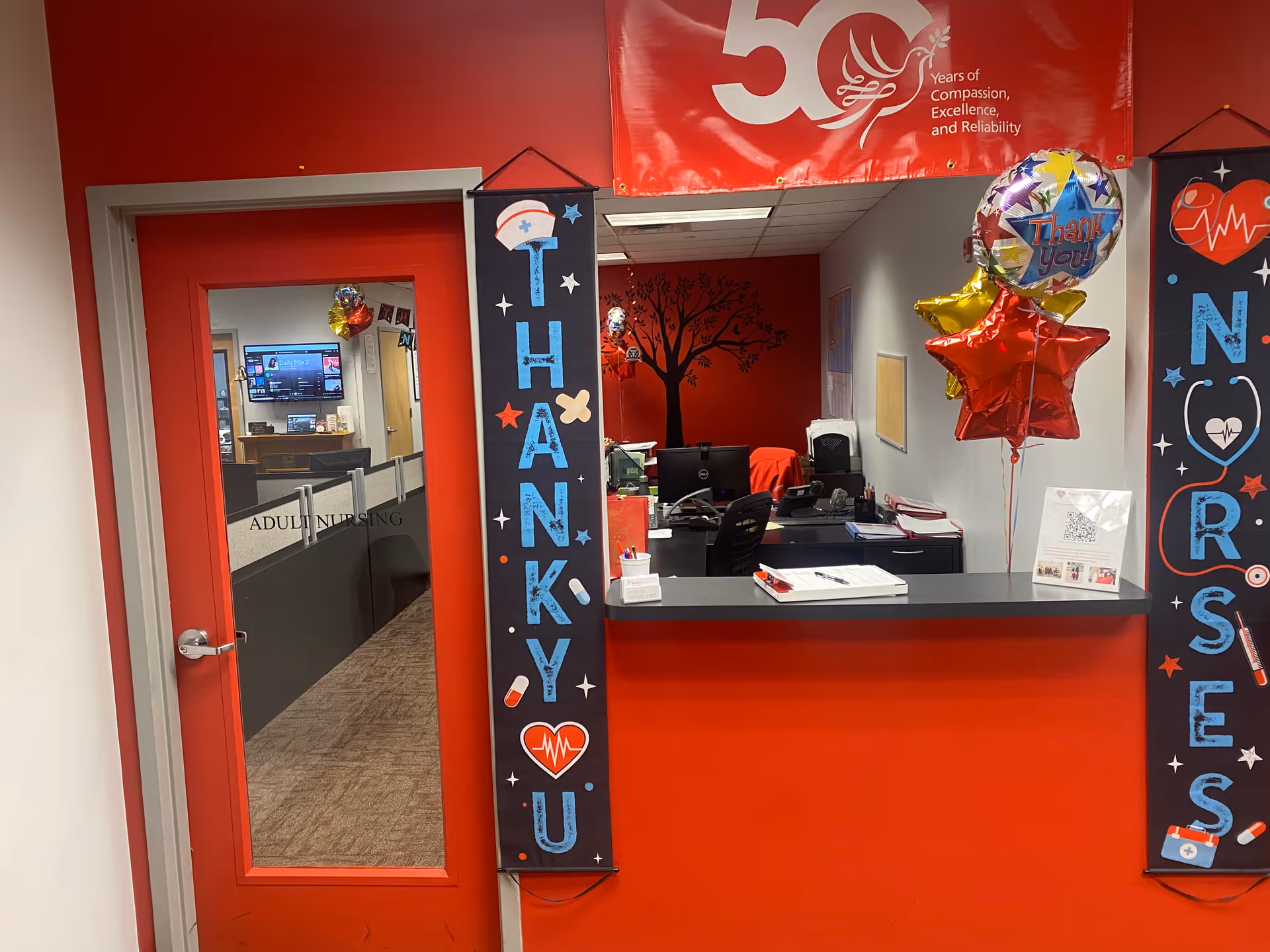 Reception desk in a BAYADA Adult Nursing facility, red decor, balloons, thank-you banners.