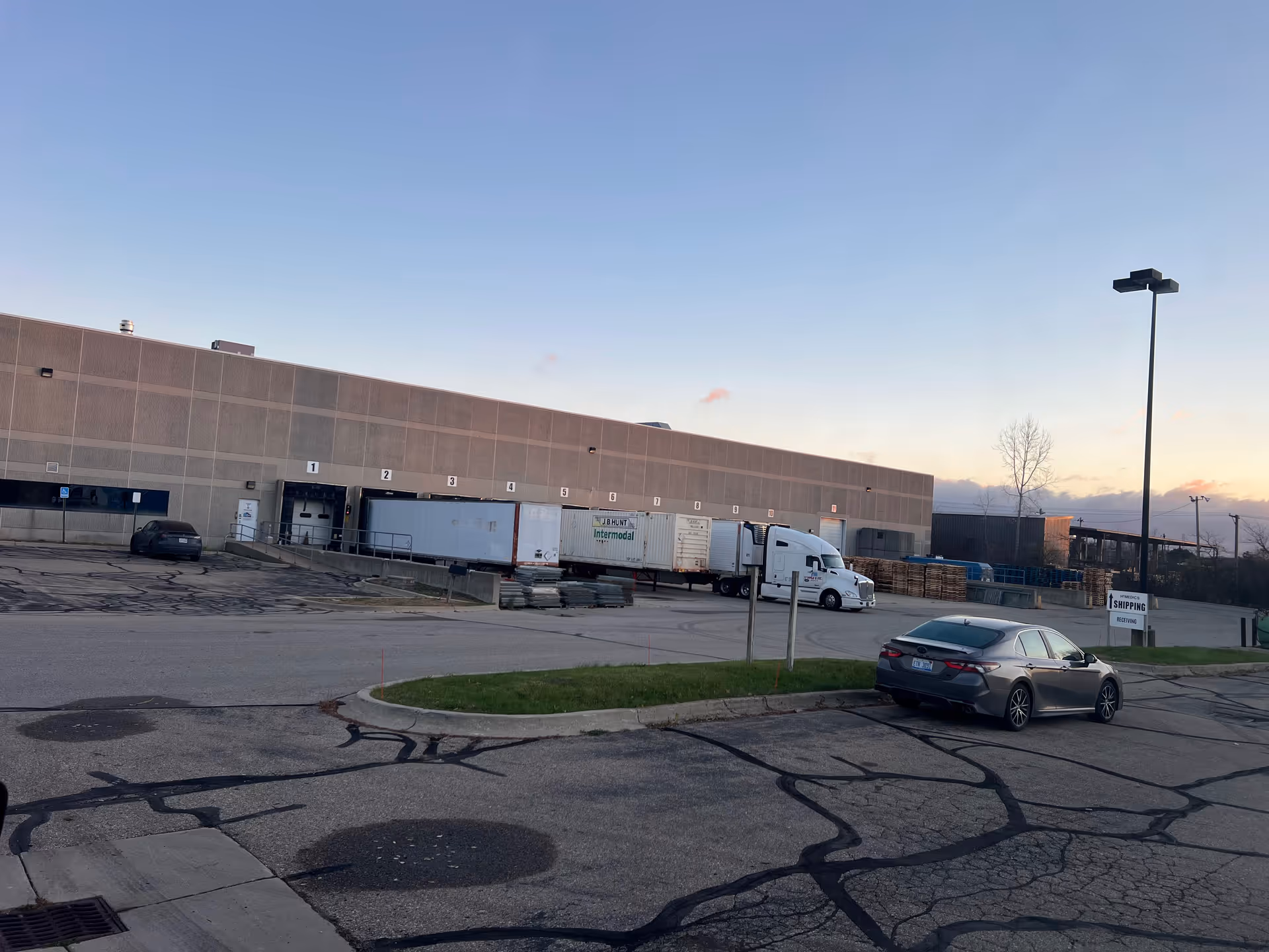 Exterior view of a large warehouse with loading docks, trucks, and a parking lot.