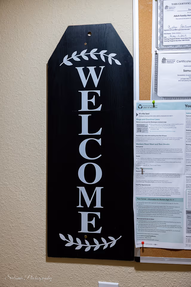 Vertical black welcome sign mounted on beige wall beside a bulletin board with papers.