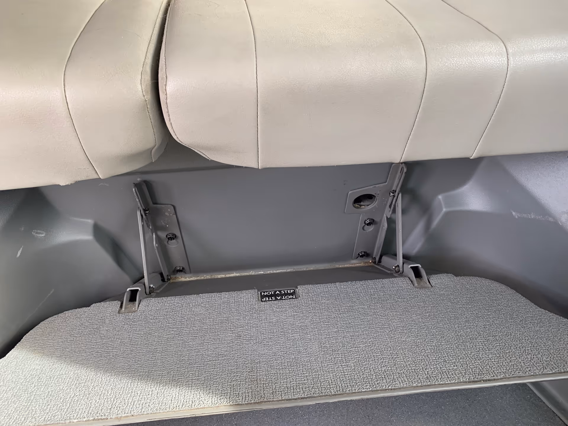 Close-up of a beige vehicle seat with mounting brackets and textured floor panel.