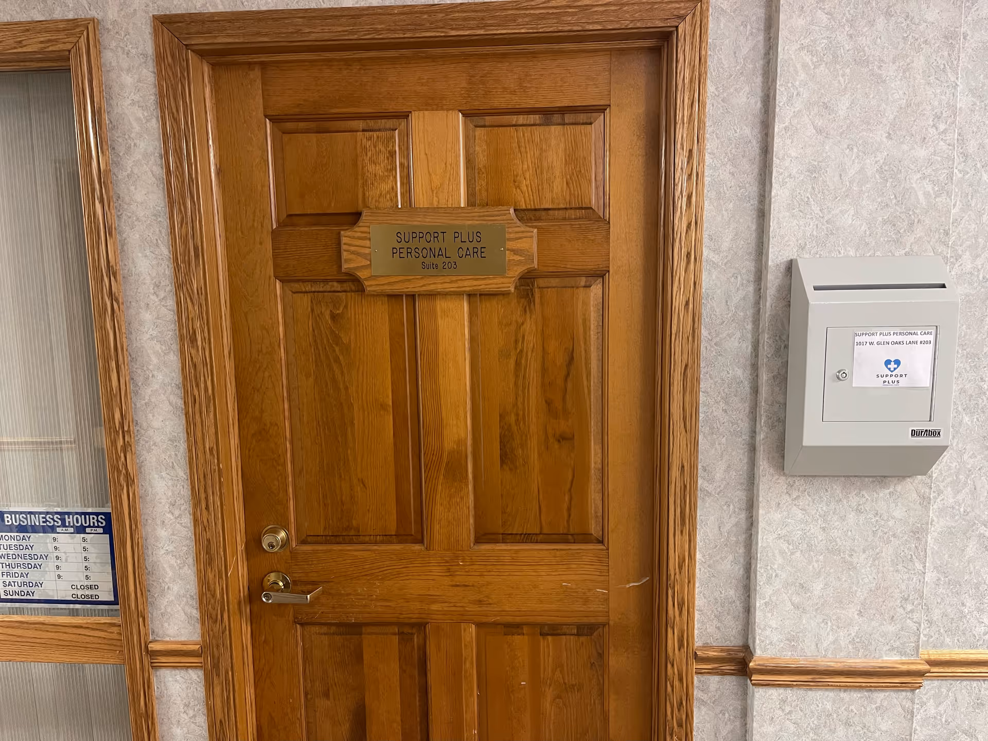Wooden interior door labeled Support Plus Personal Care in a hallway beside a wall mailbox.