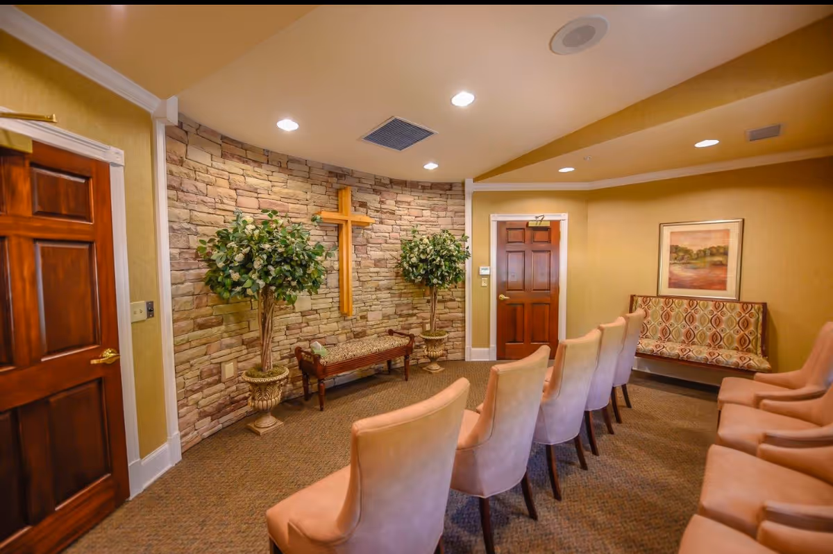 Interior chapel in a senior facility with stone wall, cross, and rows of pink chairs.