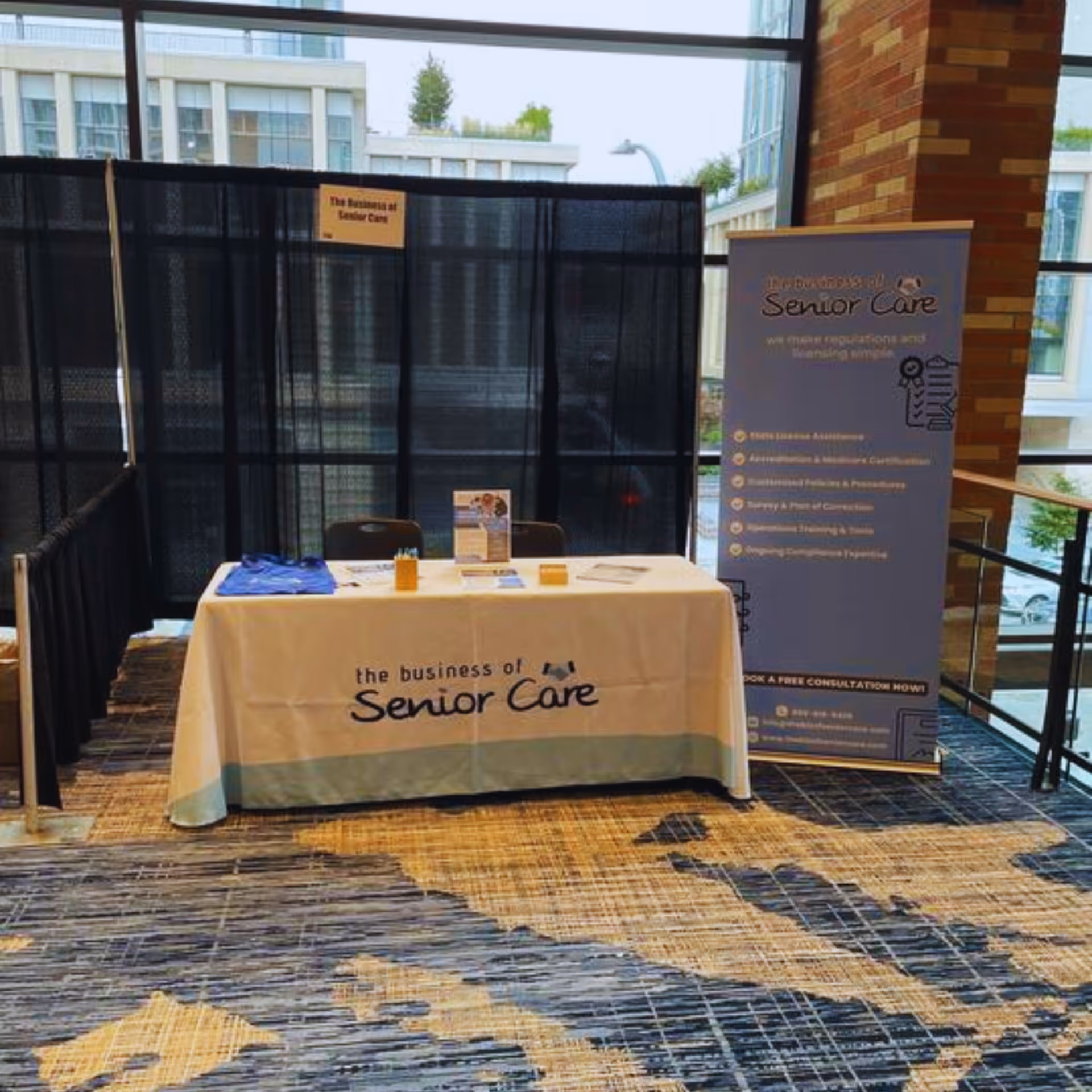 Exhibit booth with table and banner advertising The Business of Senior Care indoors.
