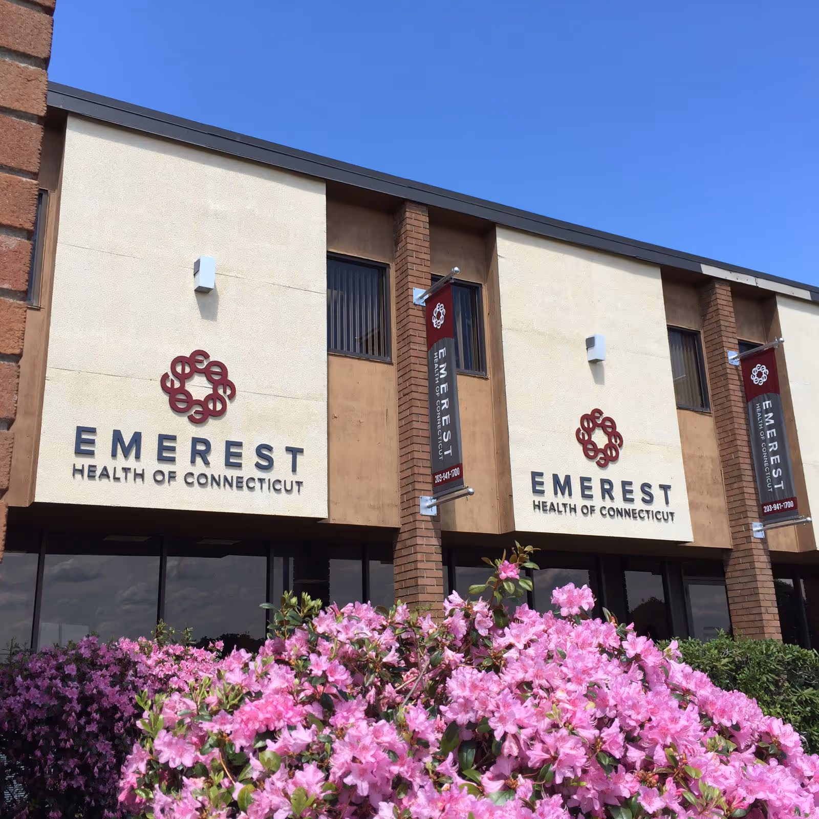 Exterior view of Emerest Health of Connecticut building with pink flowering shrubs.