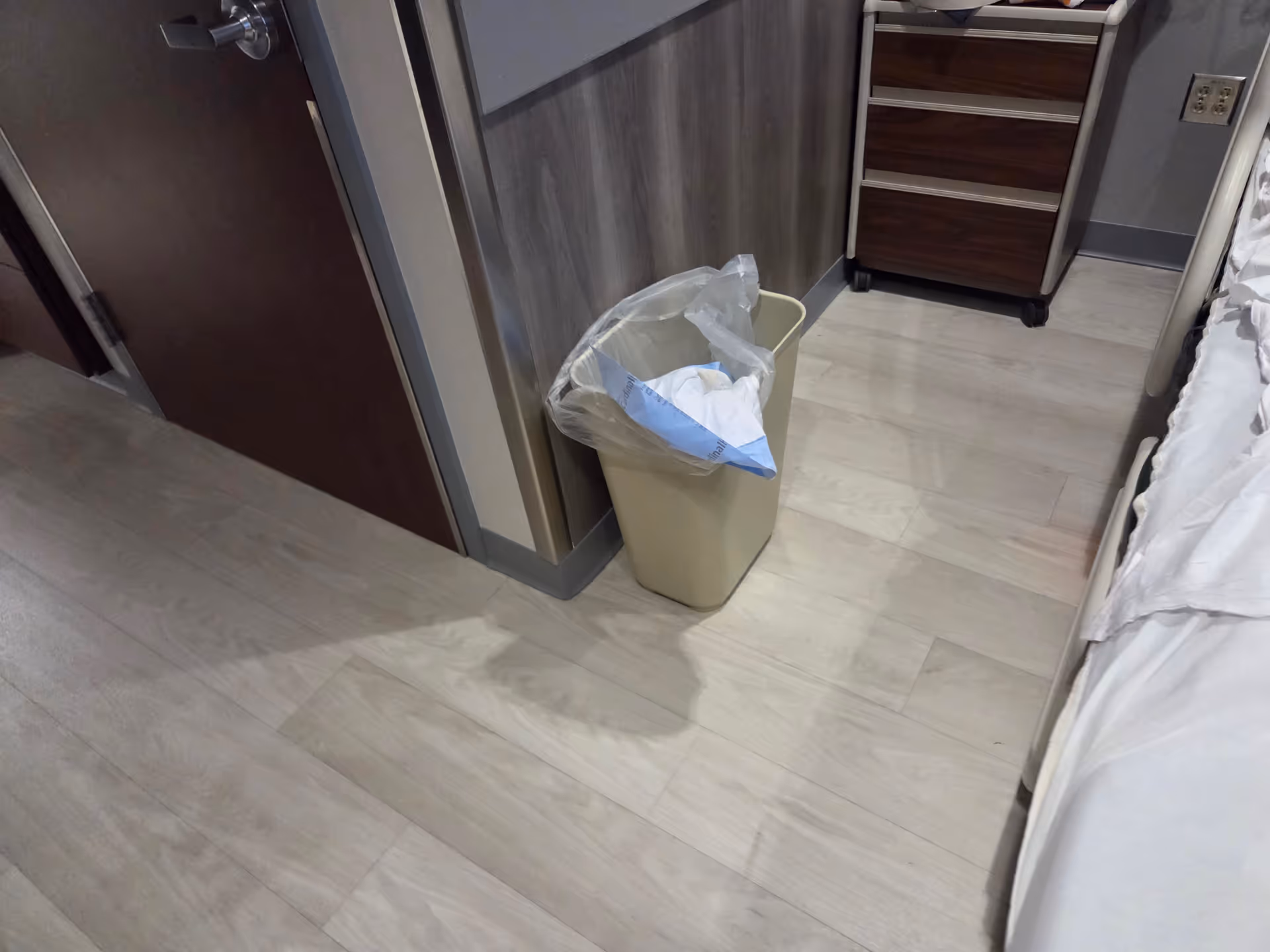 Hospital room interior with a trash can beside the bed and dresser.