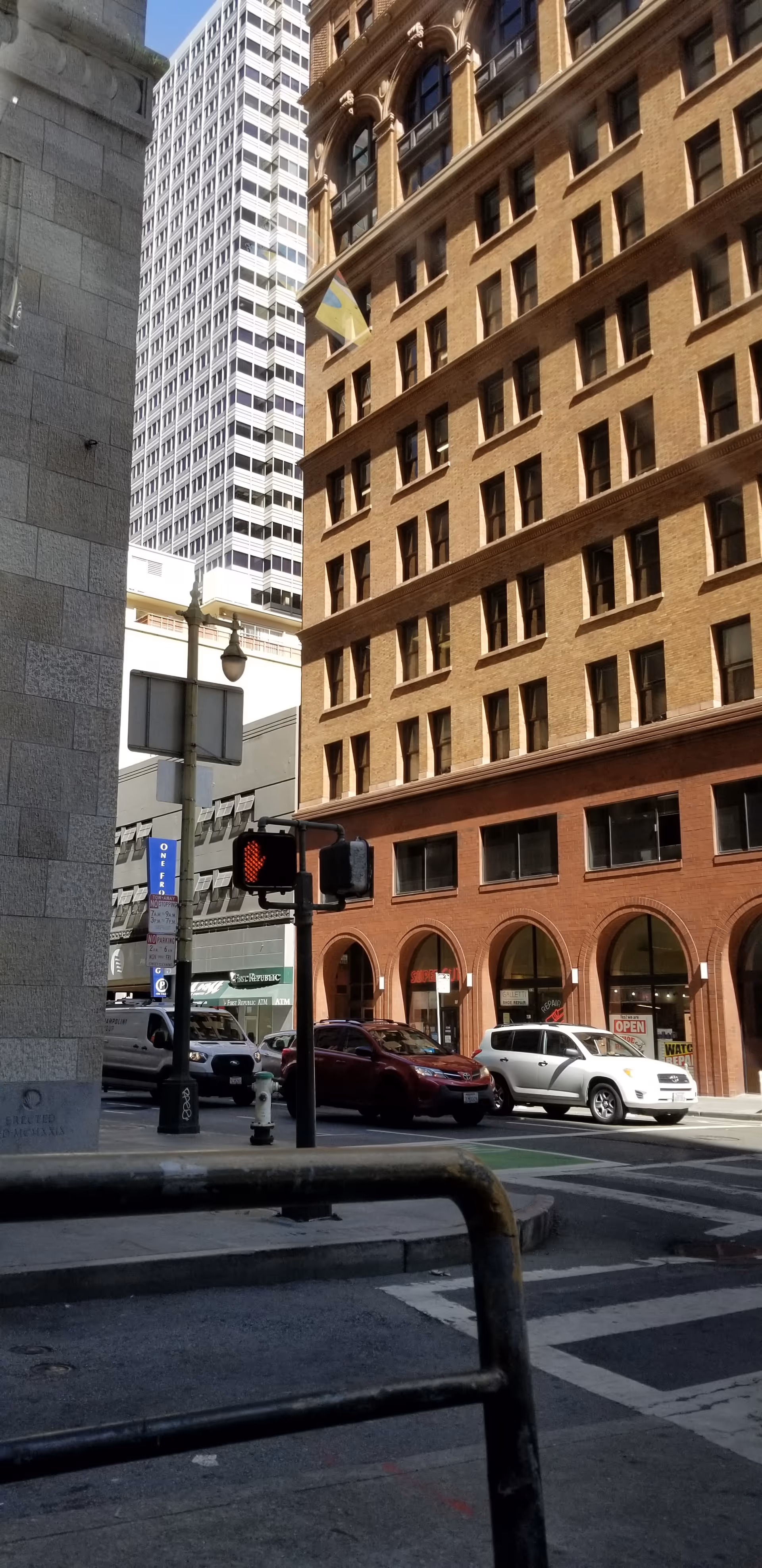 Urban street scene with tall brick and glass buildings, cars, and a crosswalk.