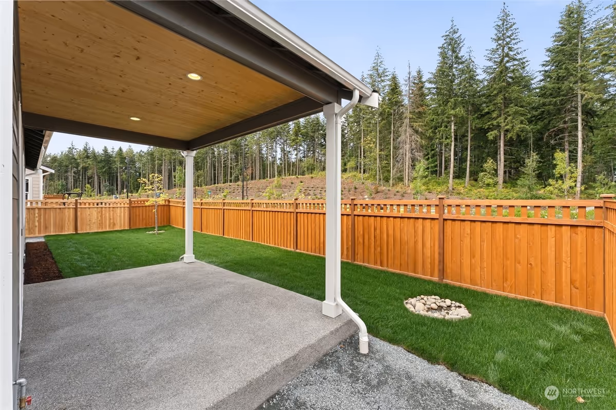 Covered patio overlooking a grassy backyard with a wooden fence and forest beyond.
