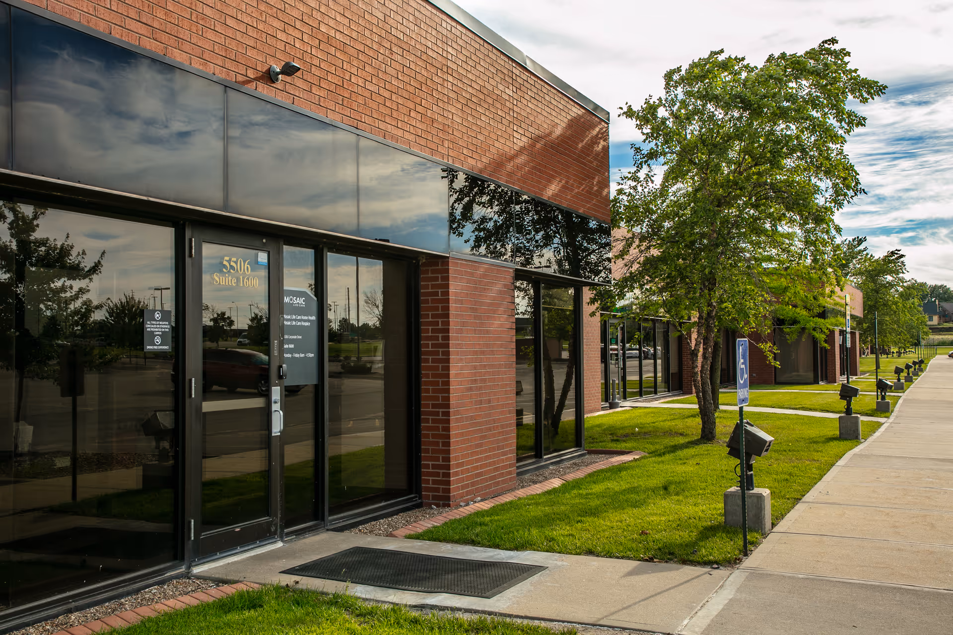 Brick building with glass entrance, a sidewalk, and trees along the front.
