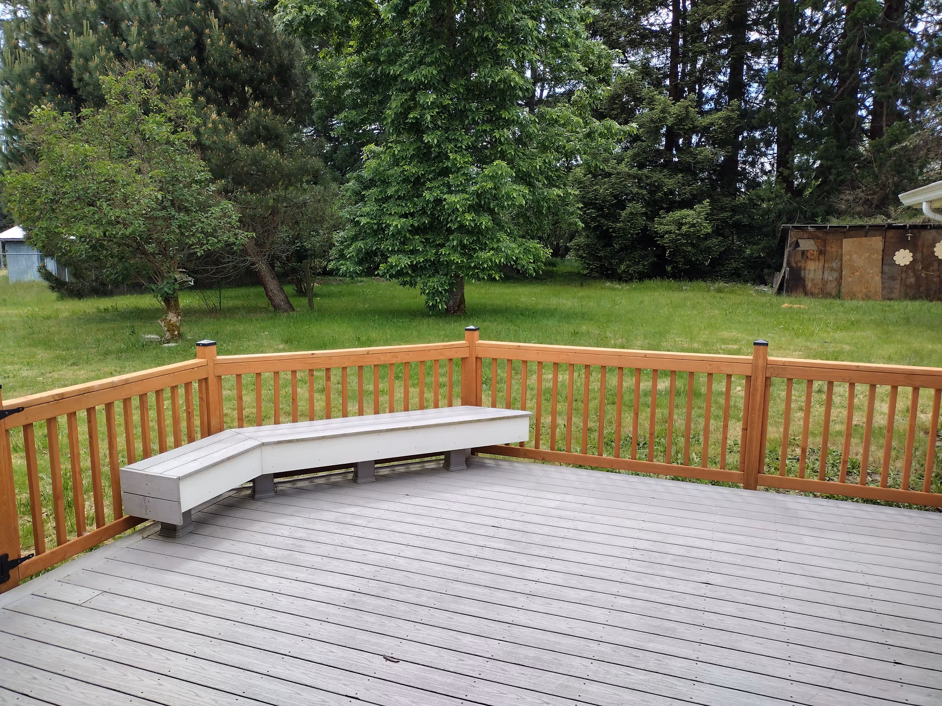 An outdoor wooden deck with a curved built-in bench overlooks a grassy yard.