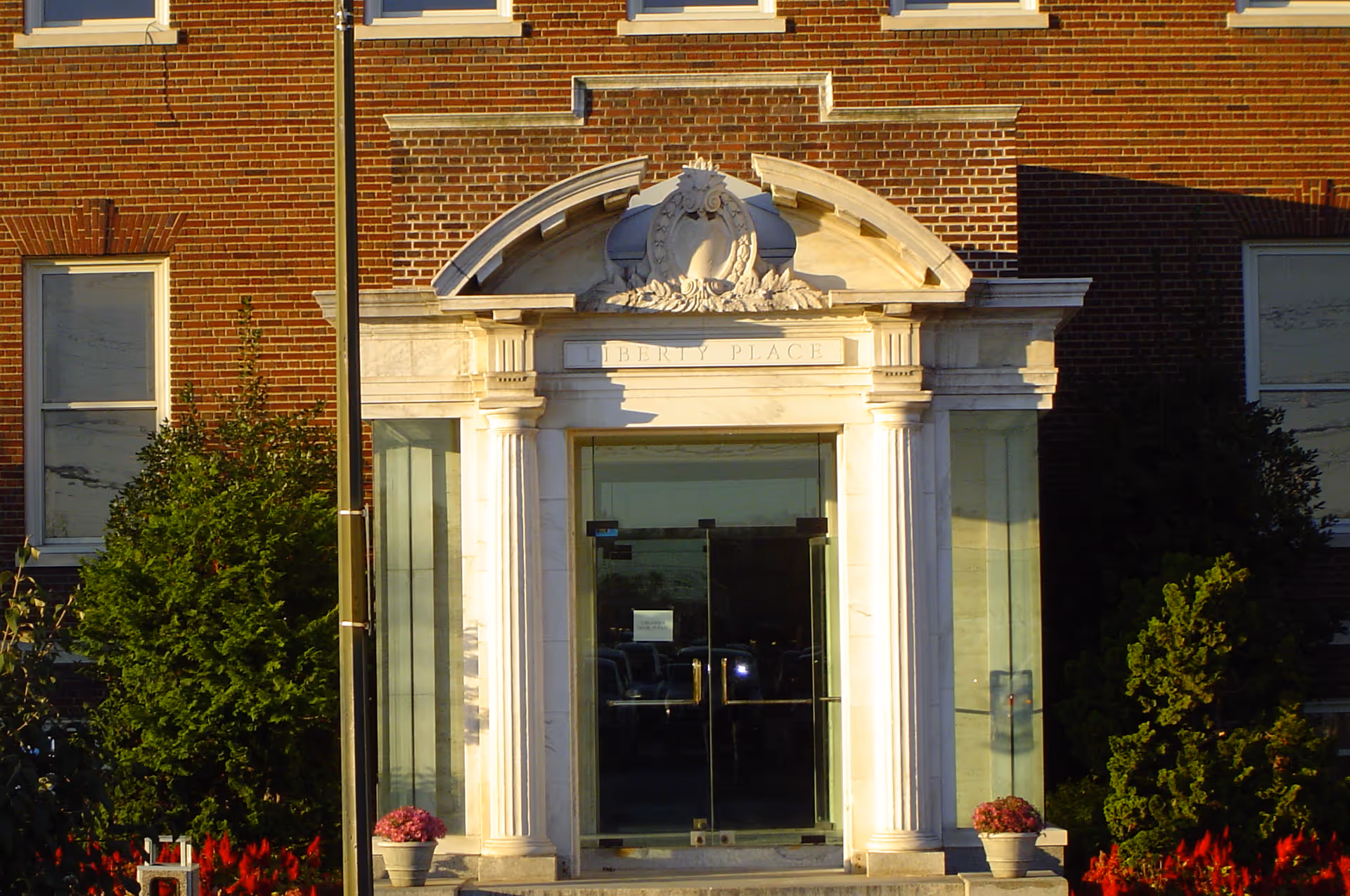 Stone entrance with tall columns and glass doors beneath a decorative arch on a brick building.