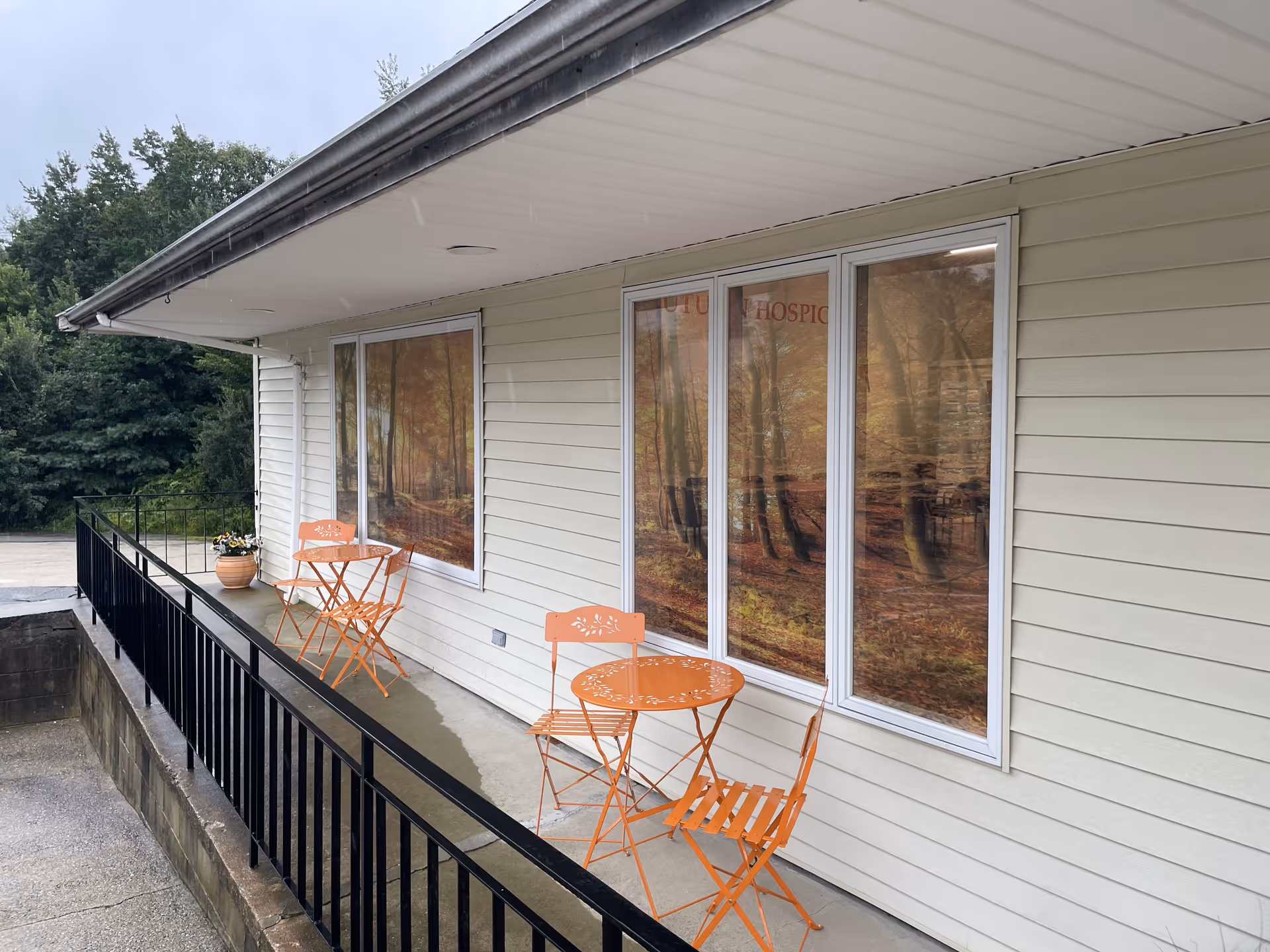 Exterior of a facility with orange outdoor seating along a railing near large windows.