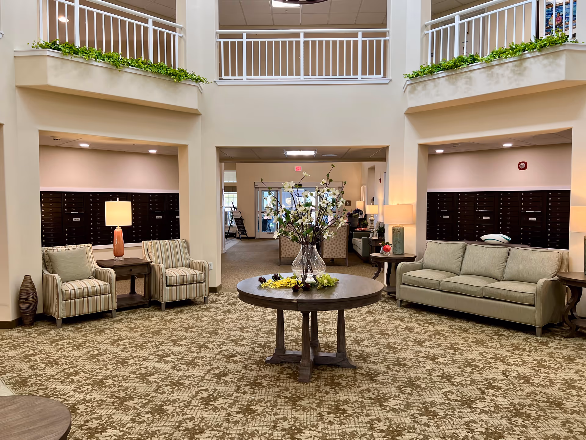 Bright lobby area with beige seating, central round table, and mailboxes.