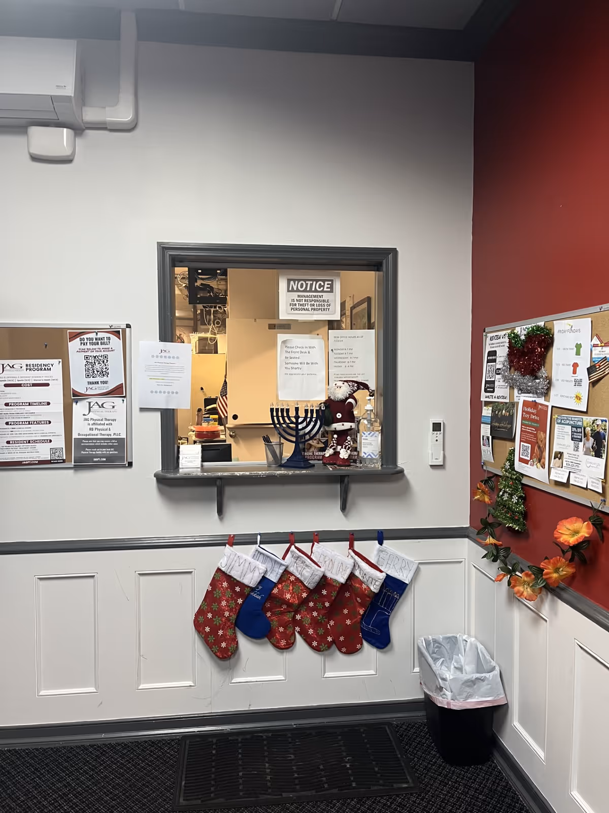 Interior facility reception window with notices, stockings, bulletin boards, and a trash can in hallway.
