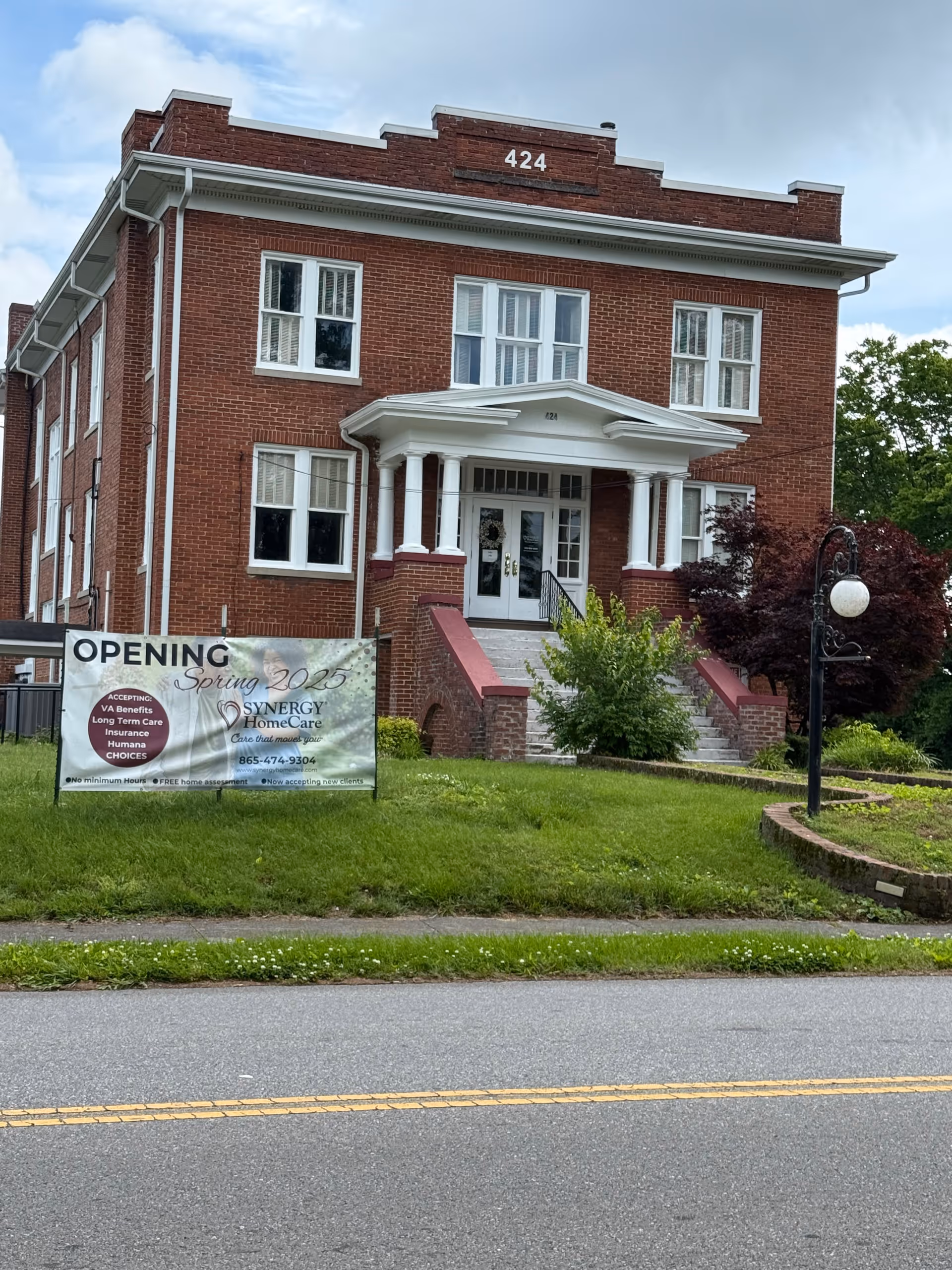 Brick two-story building with white porch entry and an opening banner on the lawn.