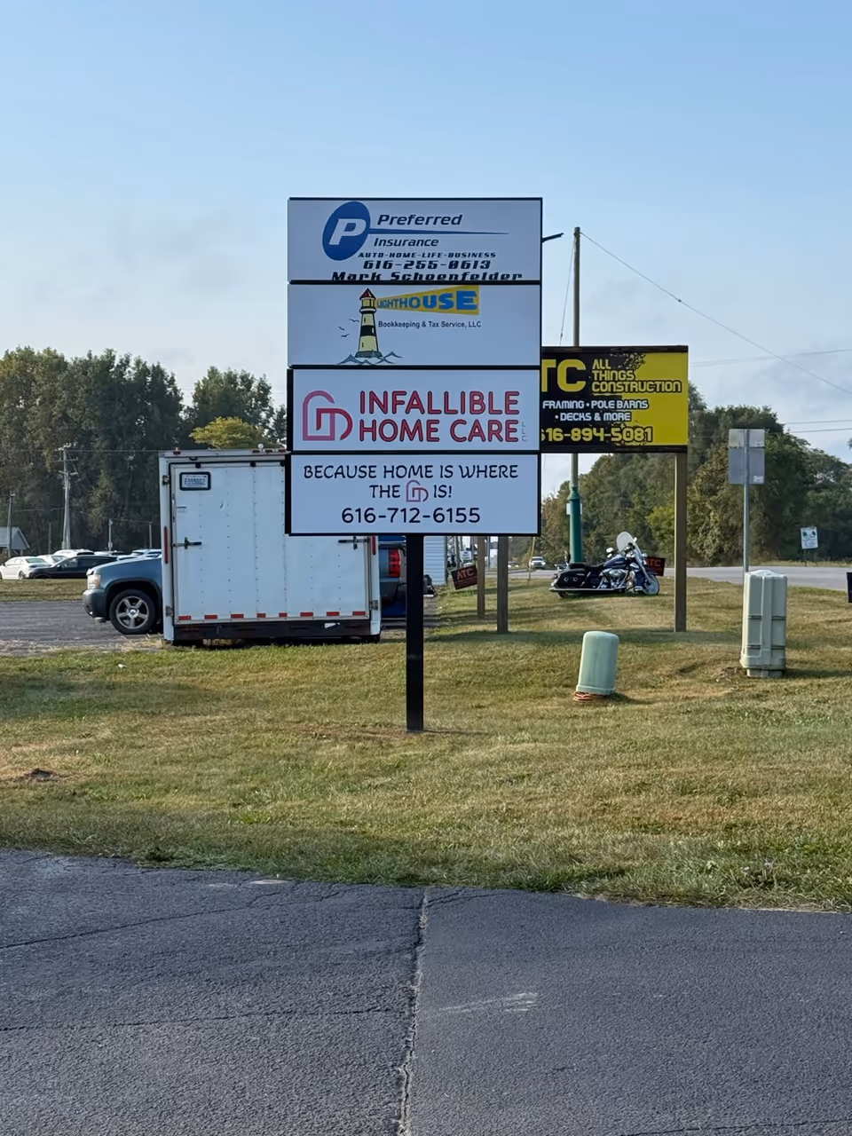 Roadside sign display for Infallible Home Care LLC with additional business signs in a grassy lot.