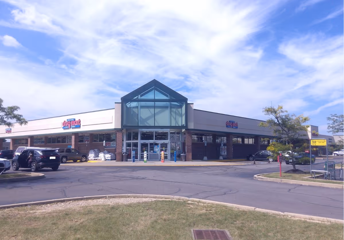 Facade of Discount Drug Mart storefront with glass atrium and parking lot in front.