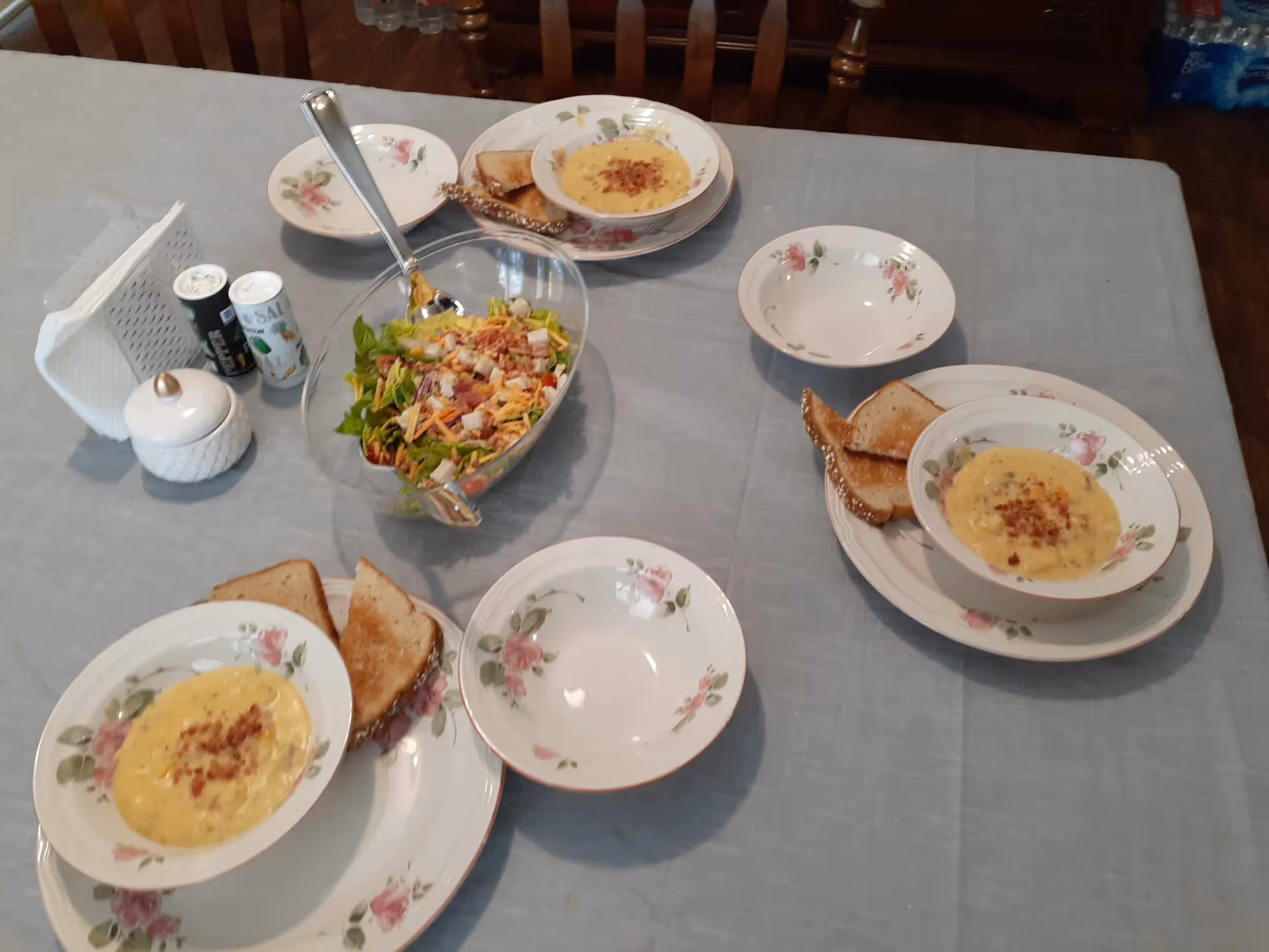 Table set for meals with soup bowls, salad, bread, and floral plates in dining room.