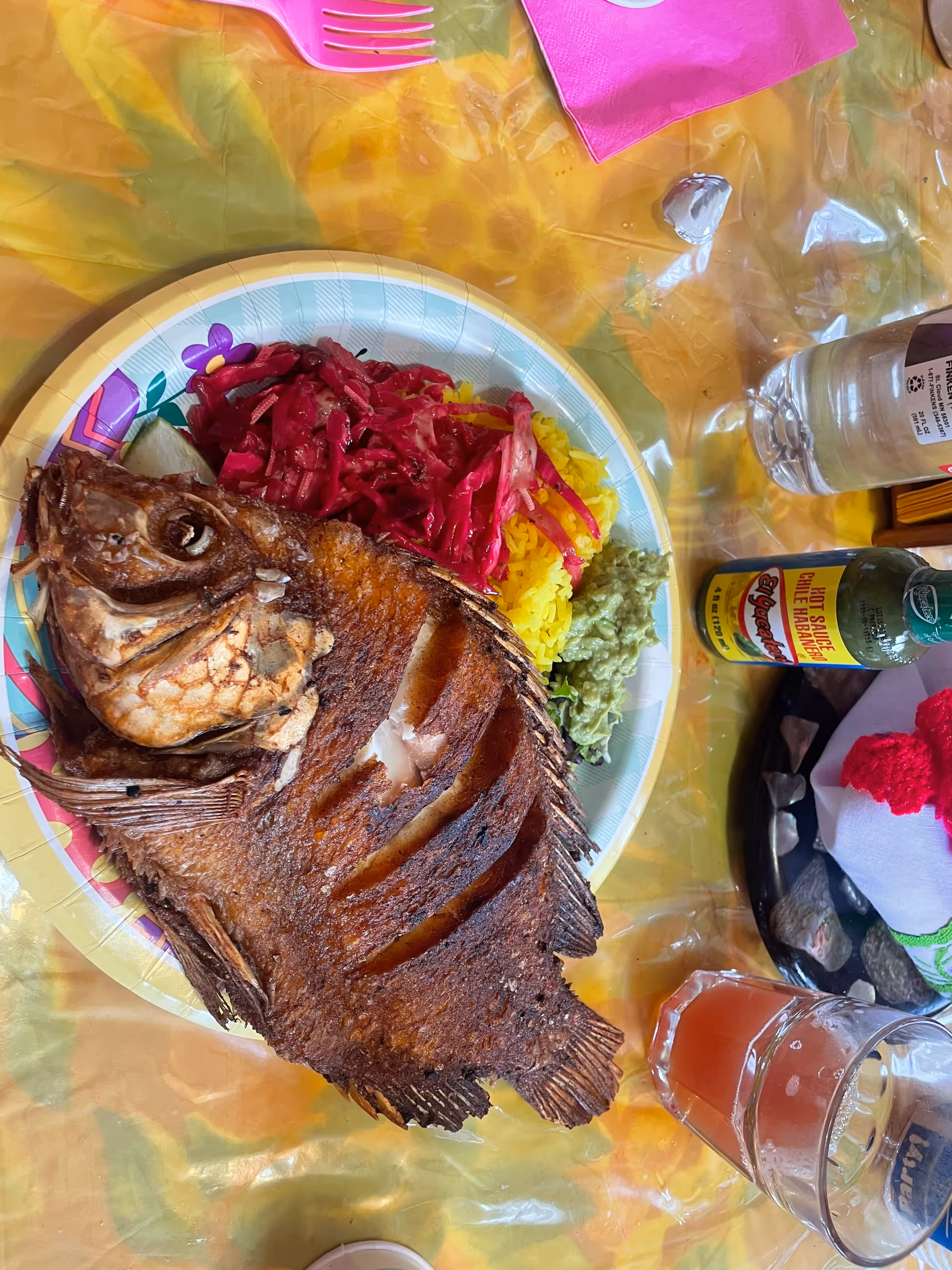 Close up of a fried fish with yellow rice and colorful sides on a dining plate.