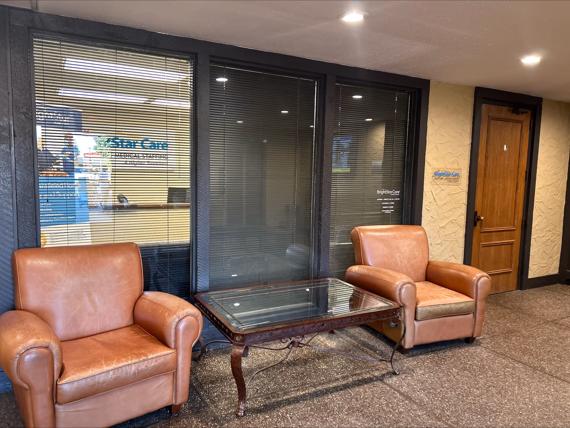 Two brown leather chairs flank a glass table in a BrightStar Care lobby.
