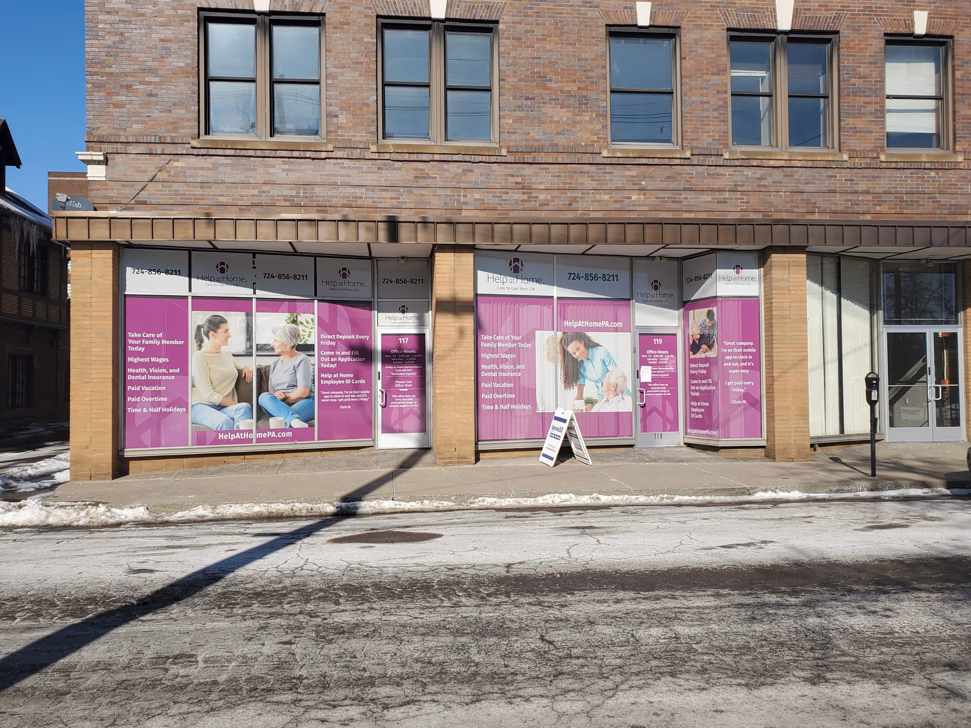 Brick building storefront with purple Help at Home advertisements along the sidewalk.