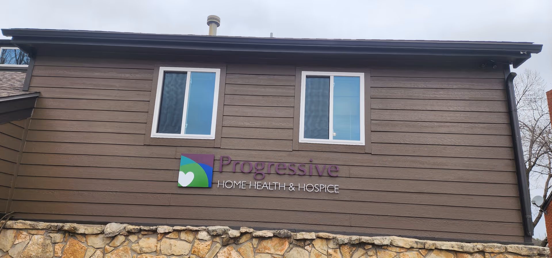 Brown siding building with a stone foundation and the Progressive Home Health & Hospice sign.