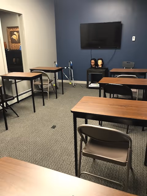 A classroom-style training room with desks, a wall-mounted TV, and mannequin heads.