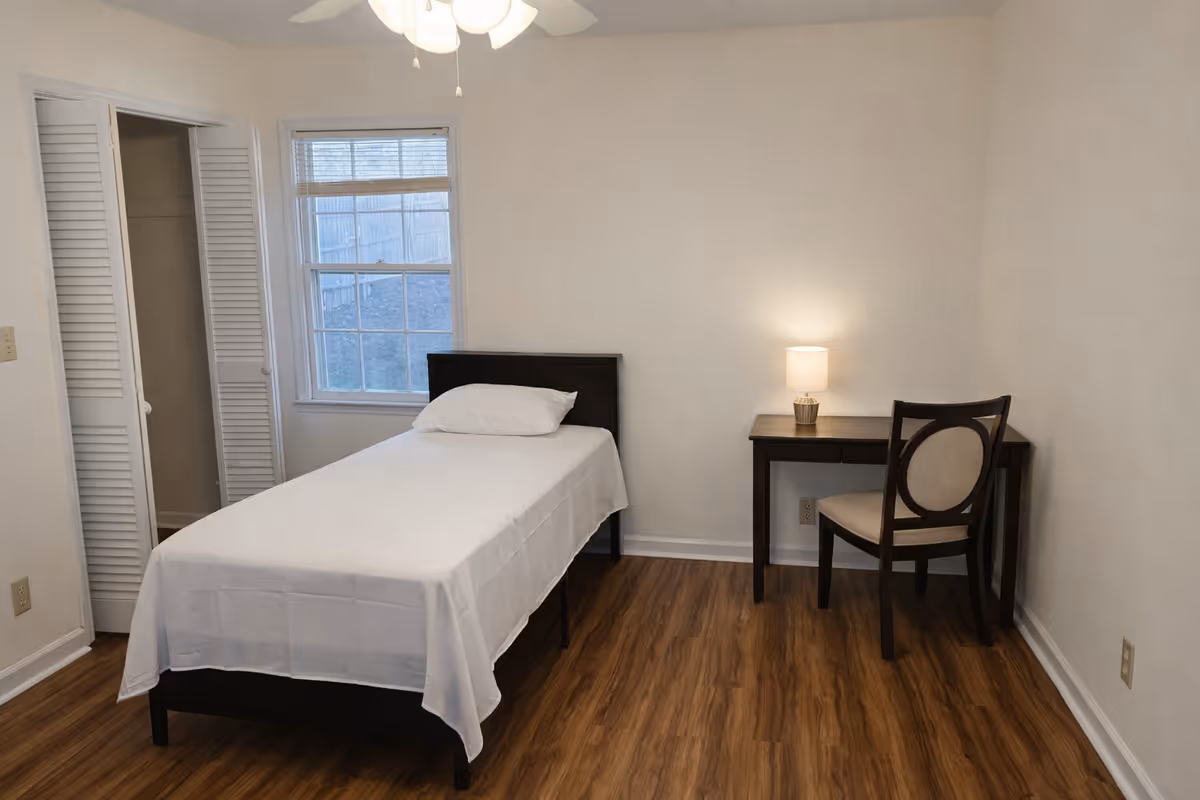 A simple bedroom with a single bed, desk, chair, and closet.