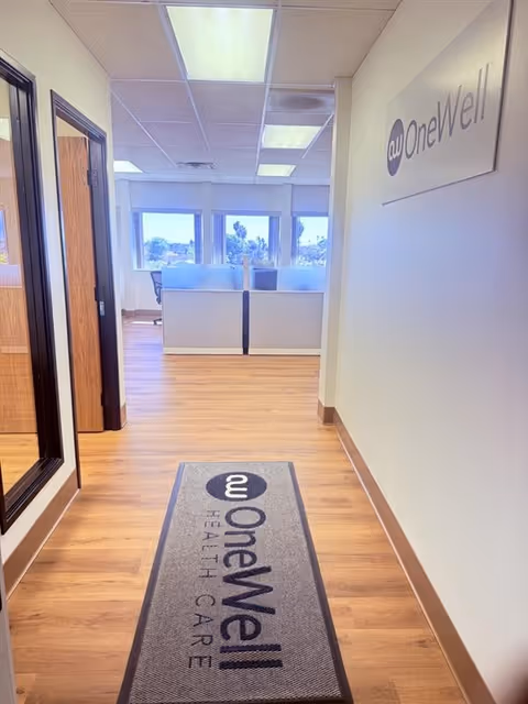 A hallway inside OneWell Health Care with a branded mat and office cubicles.