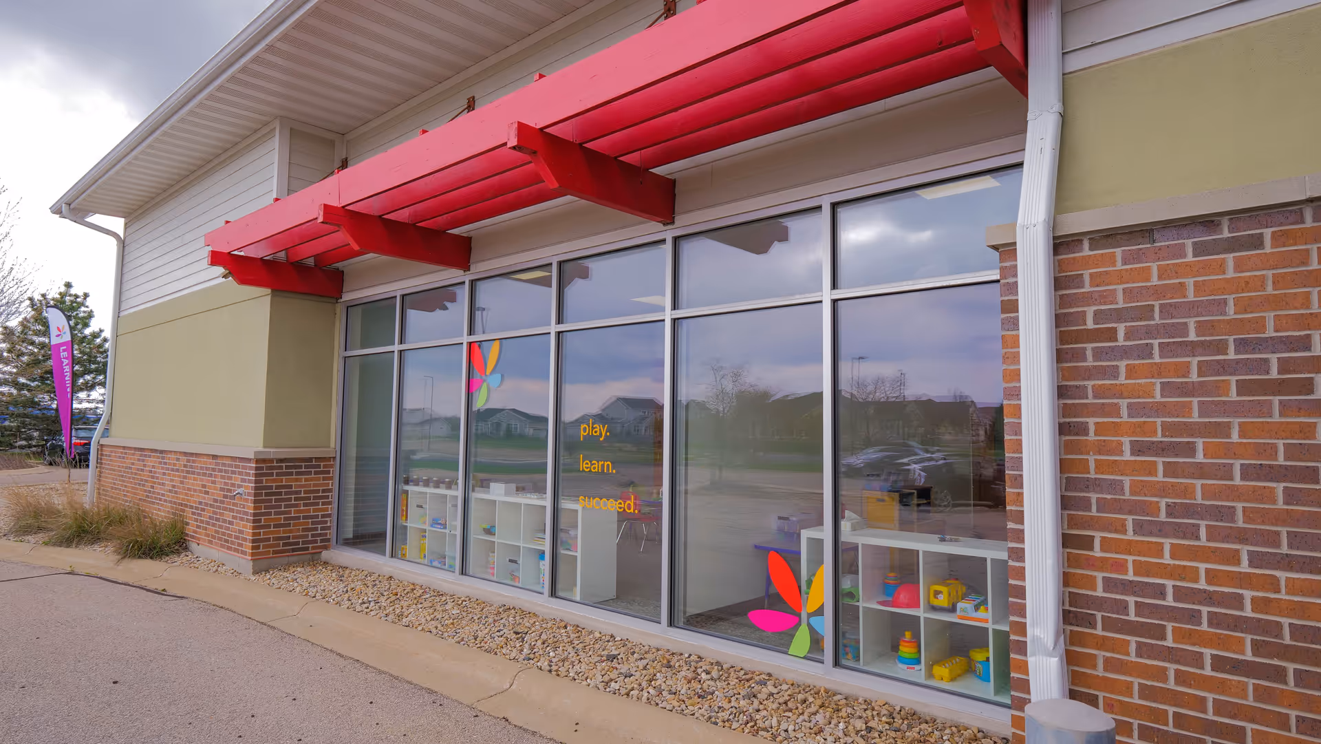 Exterior view of a WEAP facility with large glass windows, red awning, and colorful toys inside.