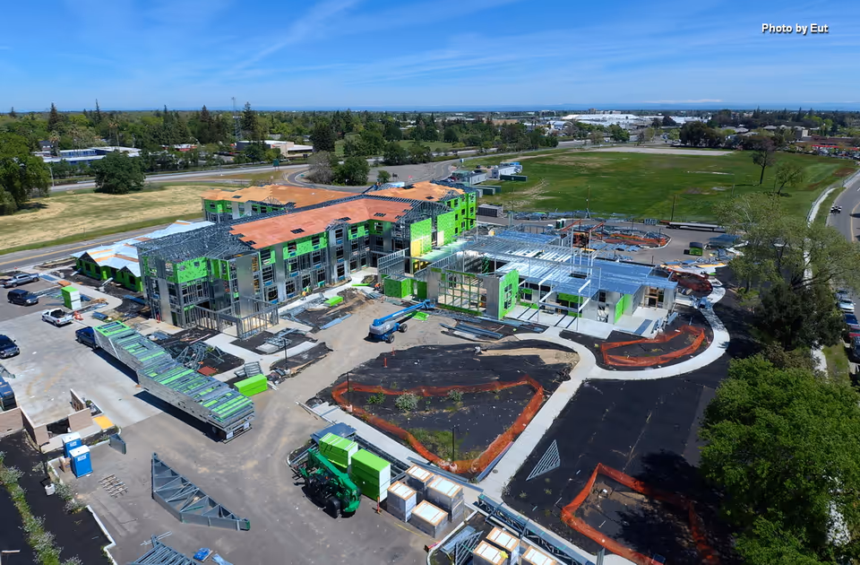 Aerial view of a large building under construction with green exterior sheathing and surrounding roads.