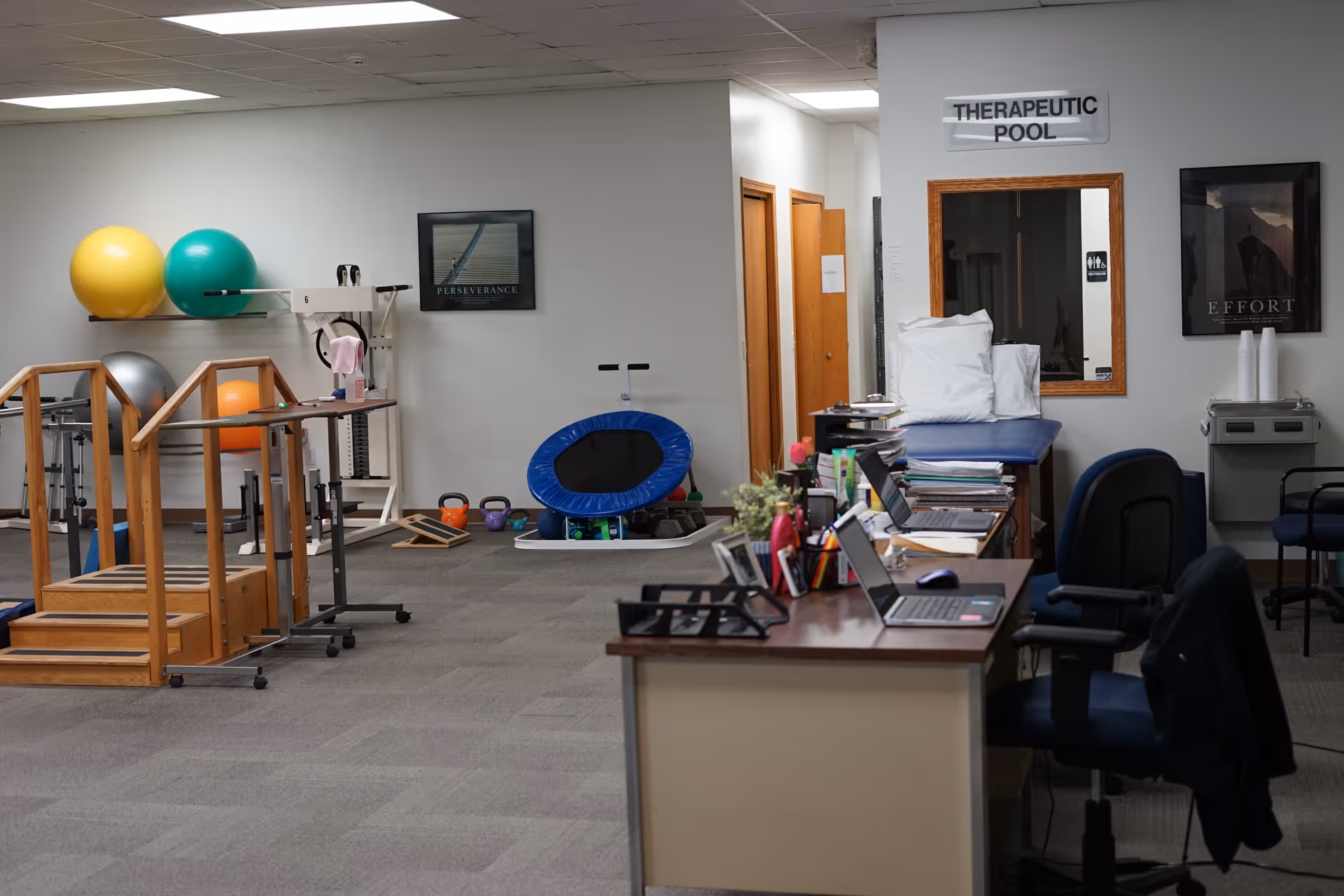 Therapy room with exercise equipment, a desk, and cushions in a clinical facility.