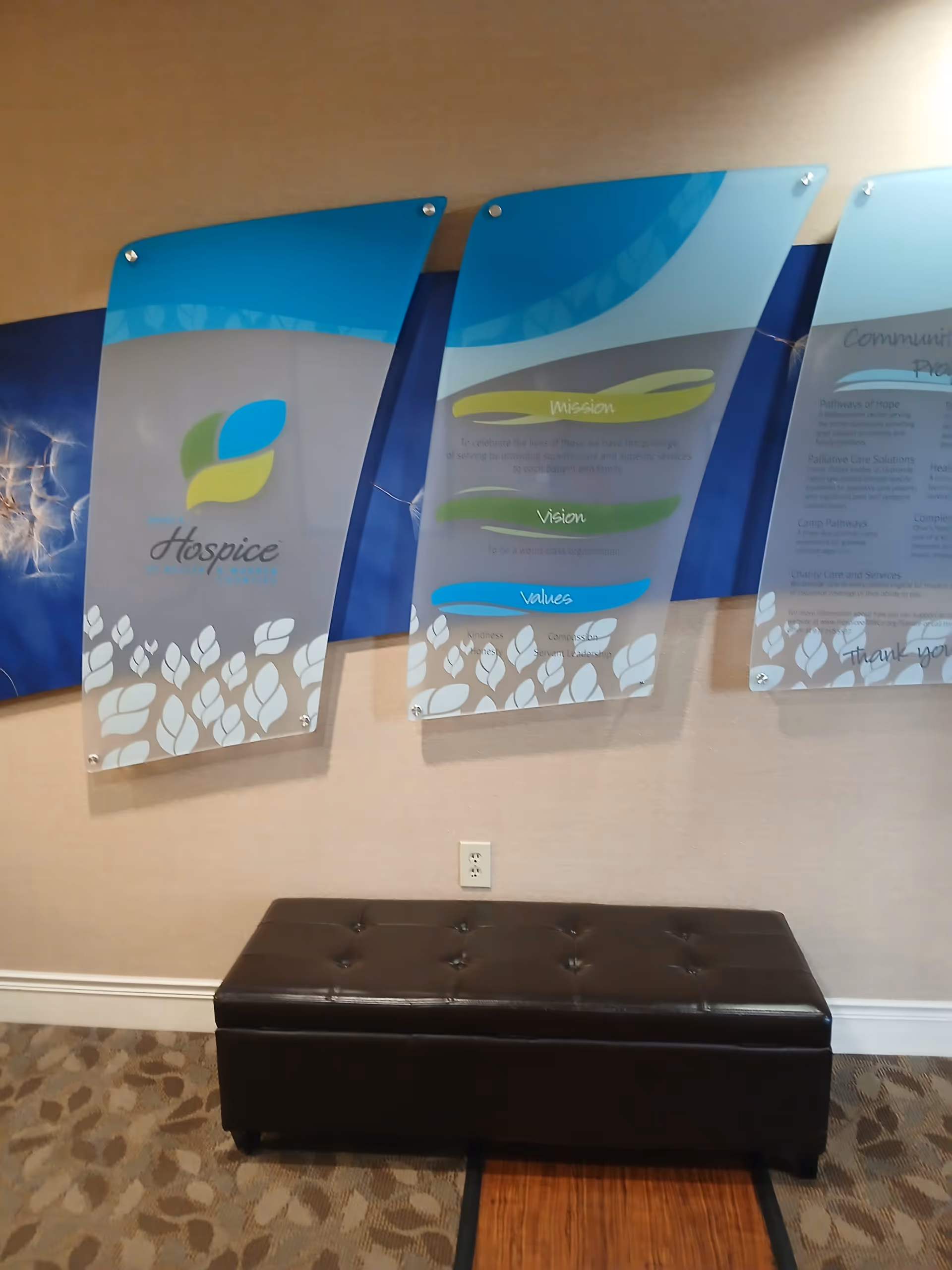 Interior lobby area with a brown tufted bench and large hospice display panels.