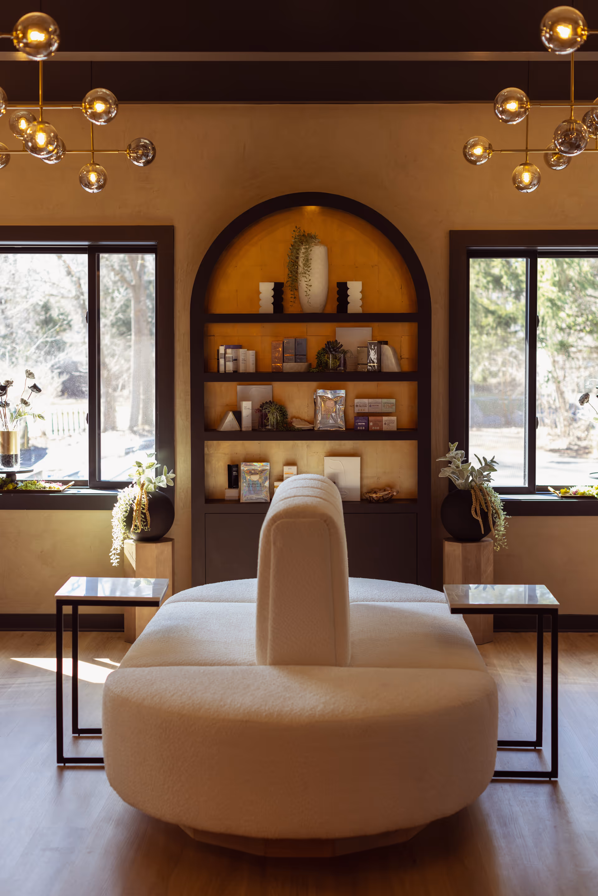 Modern wellness lounge with circular white sofa, built-in shelves, and two large windows.