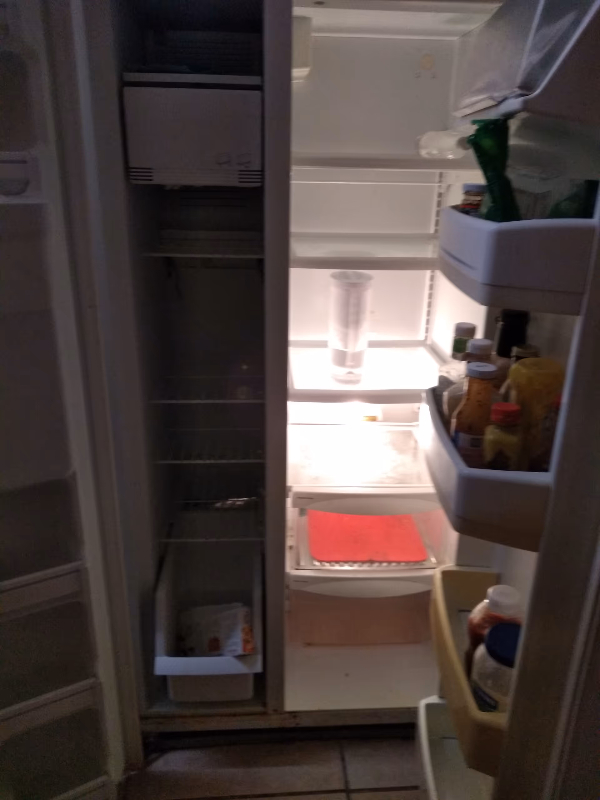 Open refrigerator with mostly empty shelves and condiments on the door in a dim kitchen.