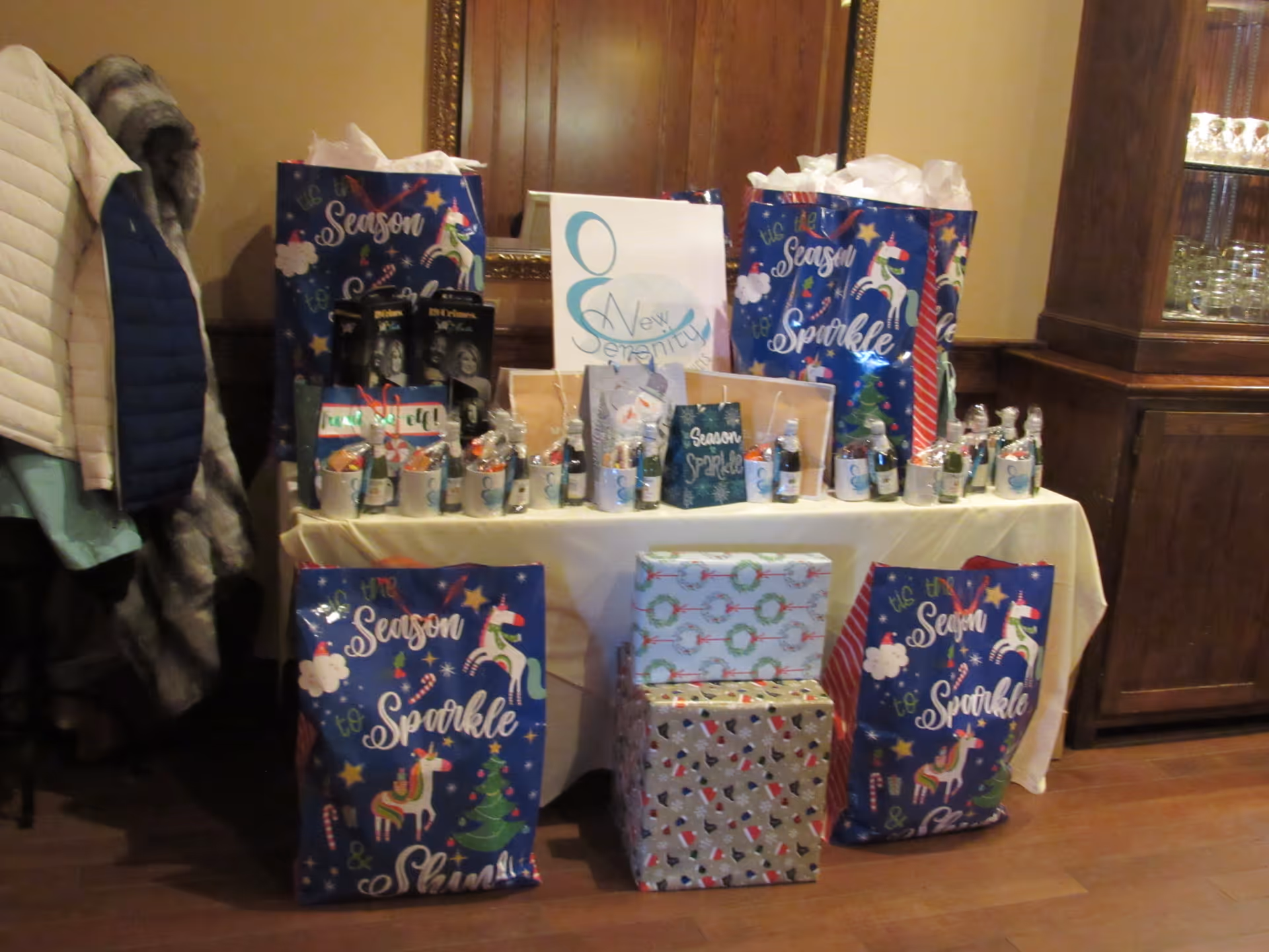 Table covered with Christmas gift bags and wrapped presents in a facility lobby.